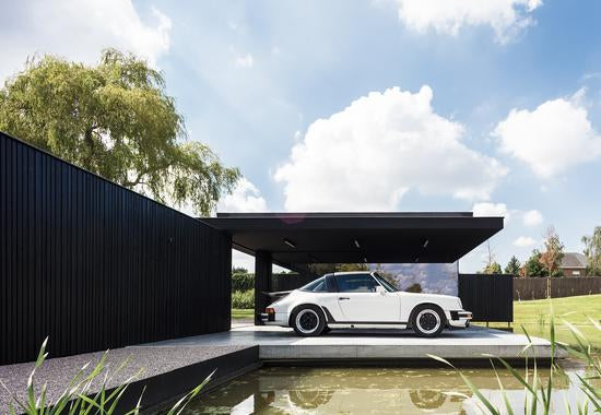Vintage white Porsche displayed next to a pond in it's architecturally designed home car port. 