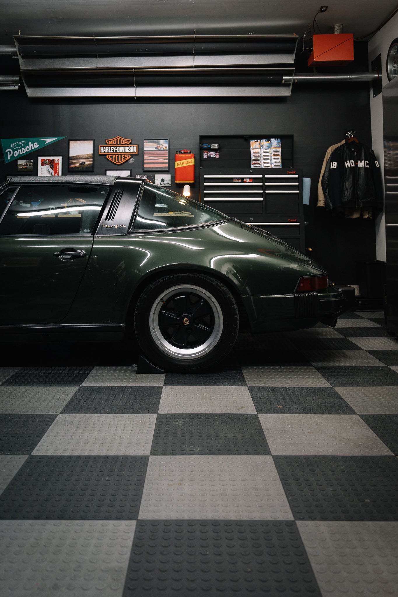 Side profile of green Porsche 911 car in a home garage with checkered floor and tool cabinet.