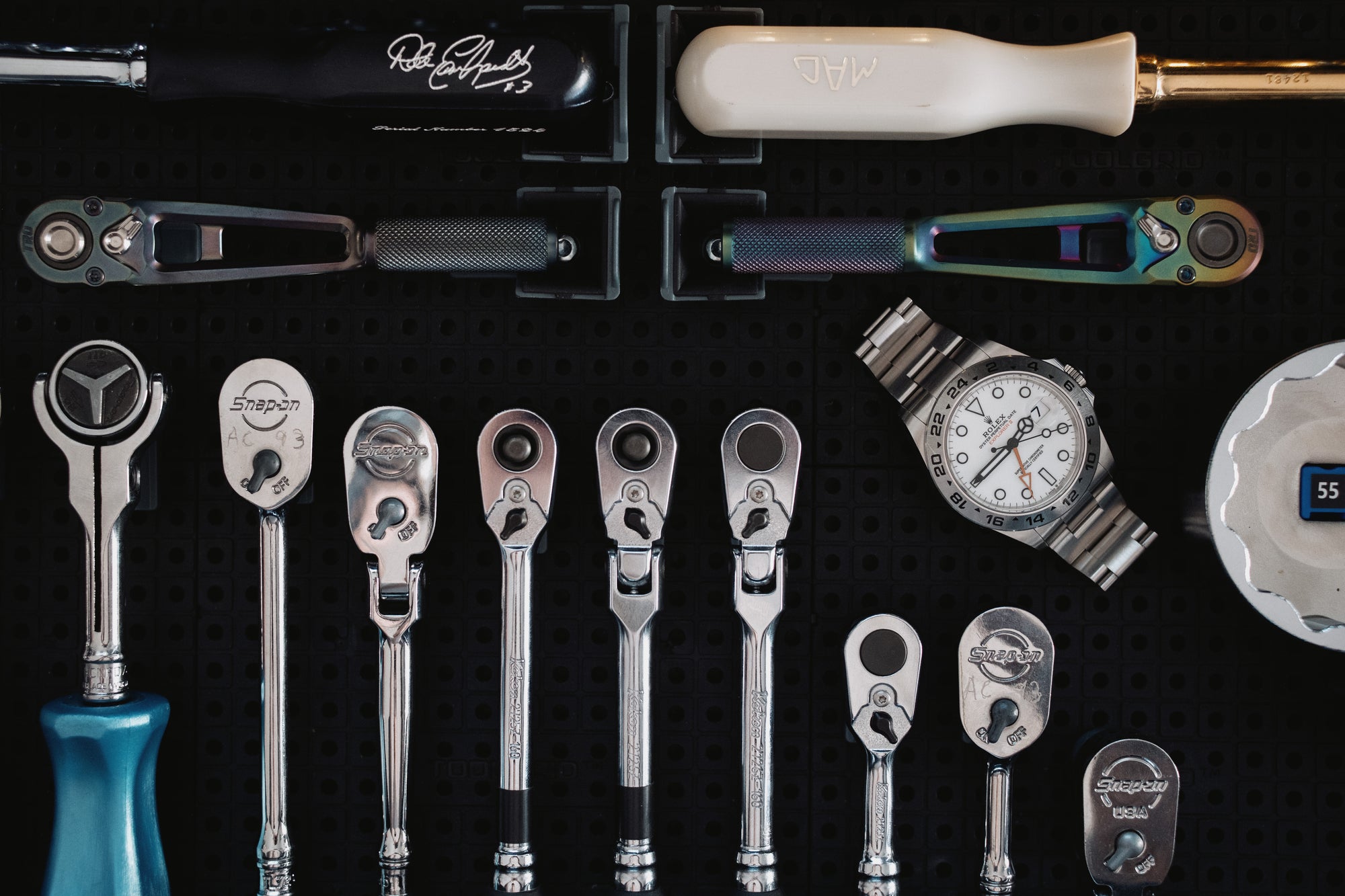 Collection of tools including wrenches, a screwdriver, Dale Earnhardt ratchet, and a Rolex Explorer watch on a dark surface.