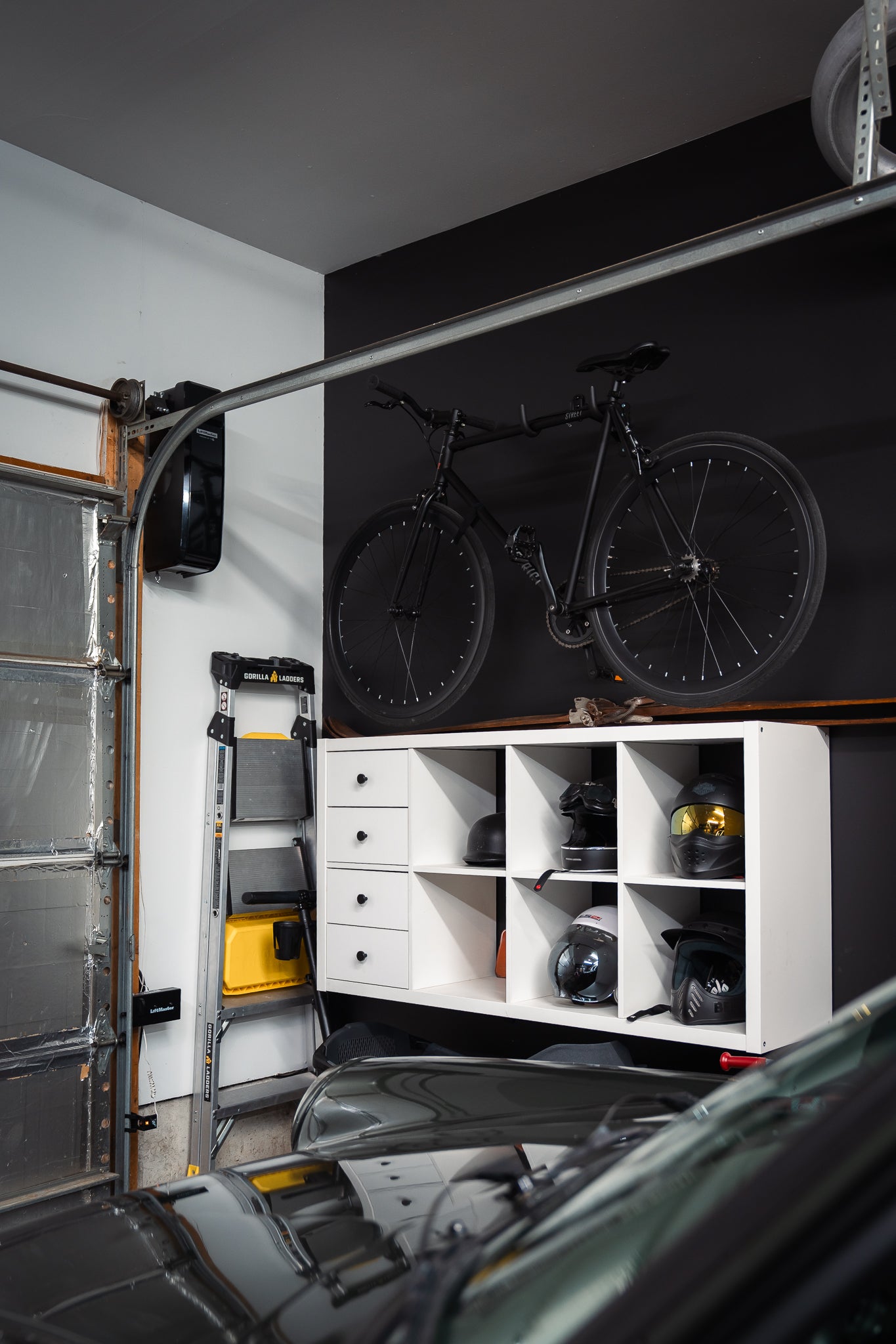 Garage interior with a bicycle hanging on the black wall, shelves with items, and a Porsche partially visible.