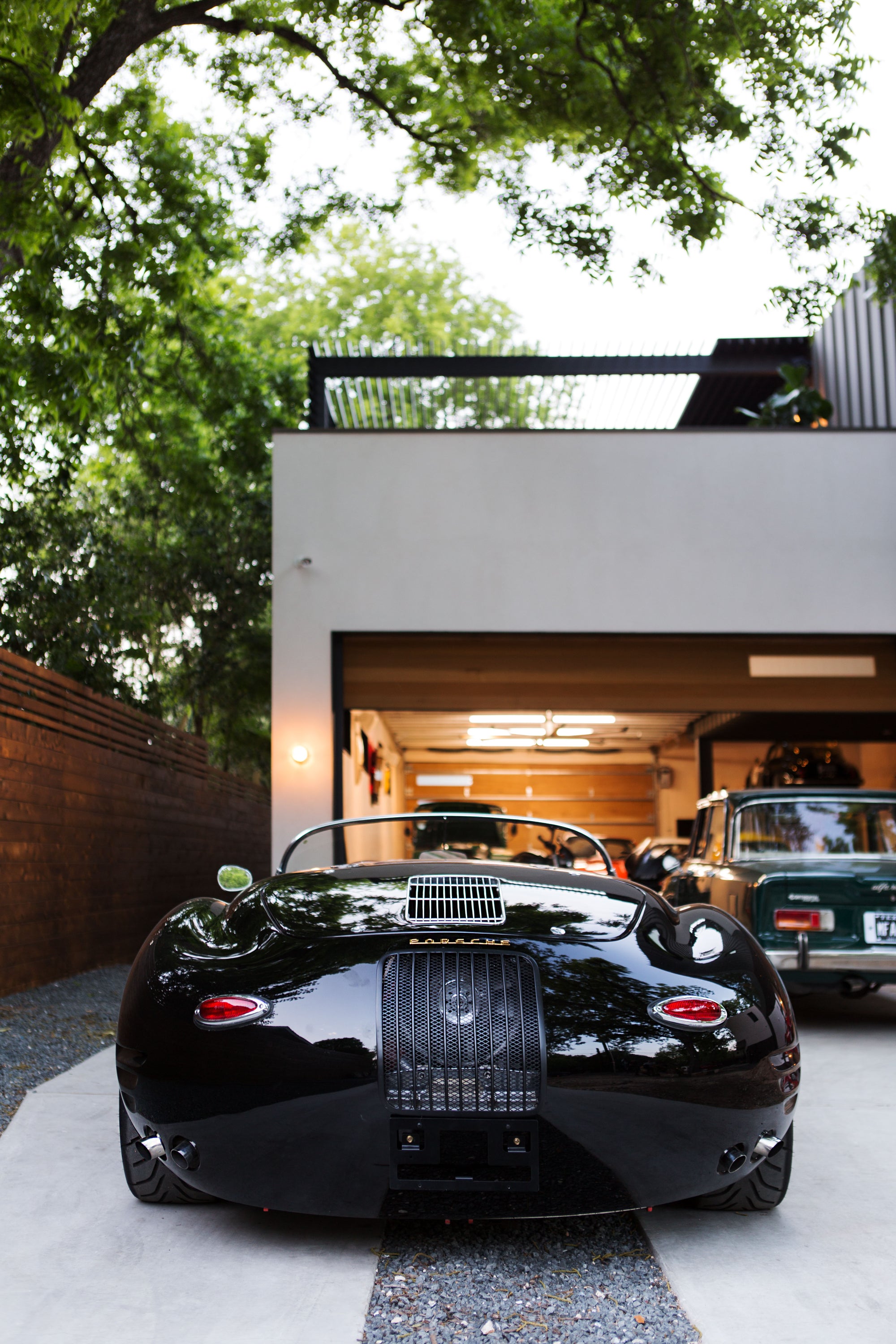 Rear view of a black vintage Porsche Speedster parked on a driveway outside a modern garage.