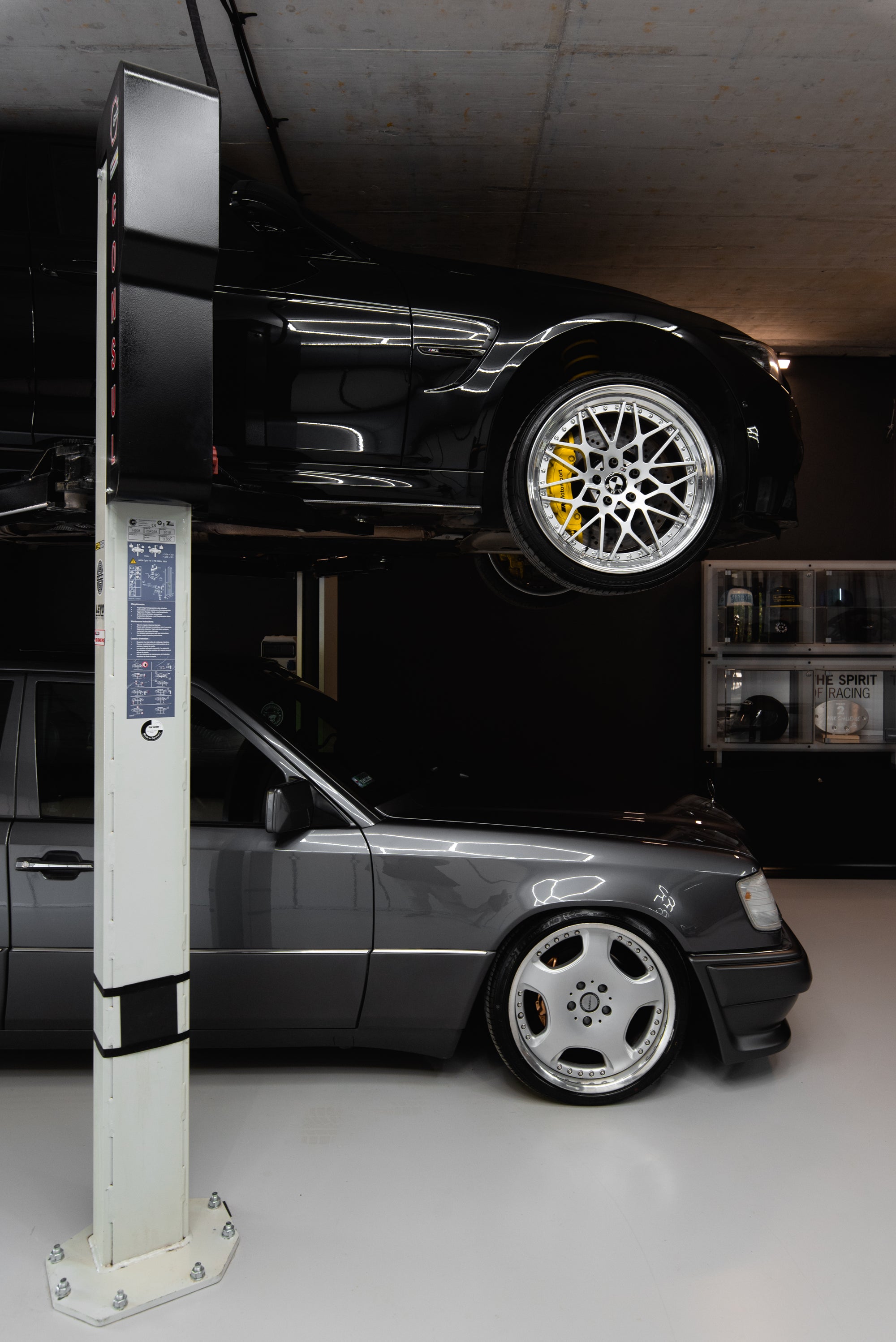 BMW M3 on car lift above classic Mercedes in a functional home garage setup