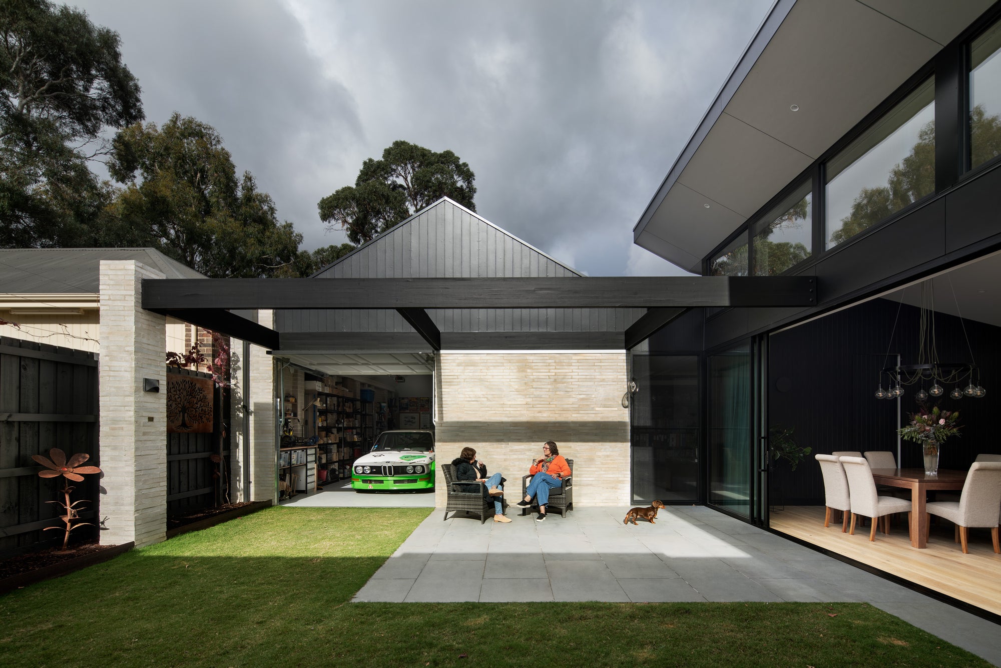 Courtyard of Campbell St House with open BMW rally car workshop visible and couple seated alfresco in Kew