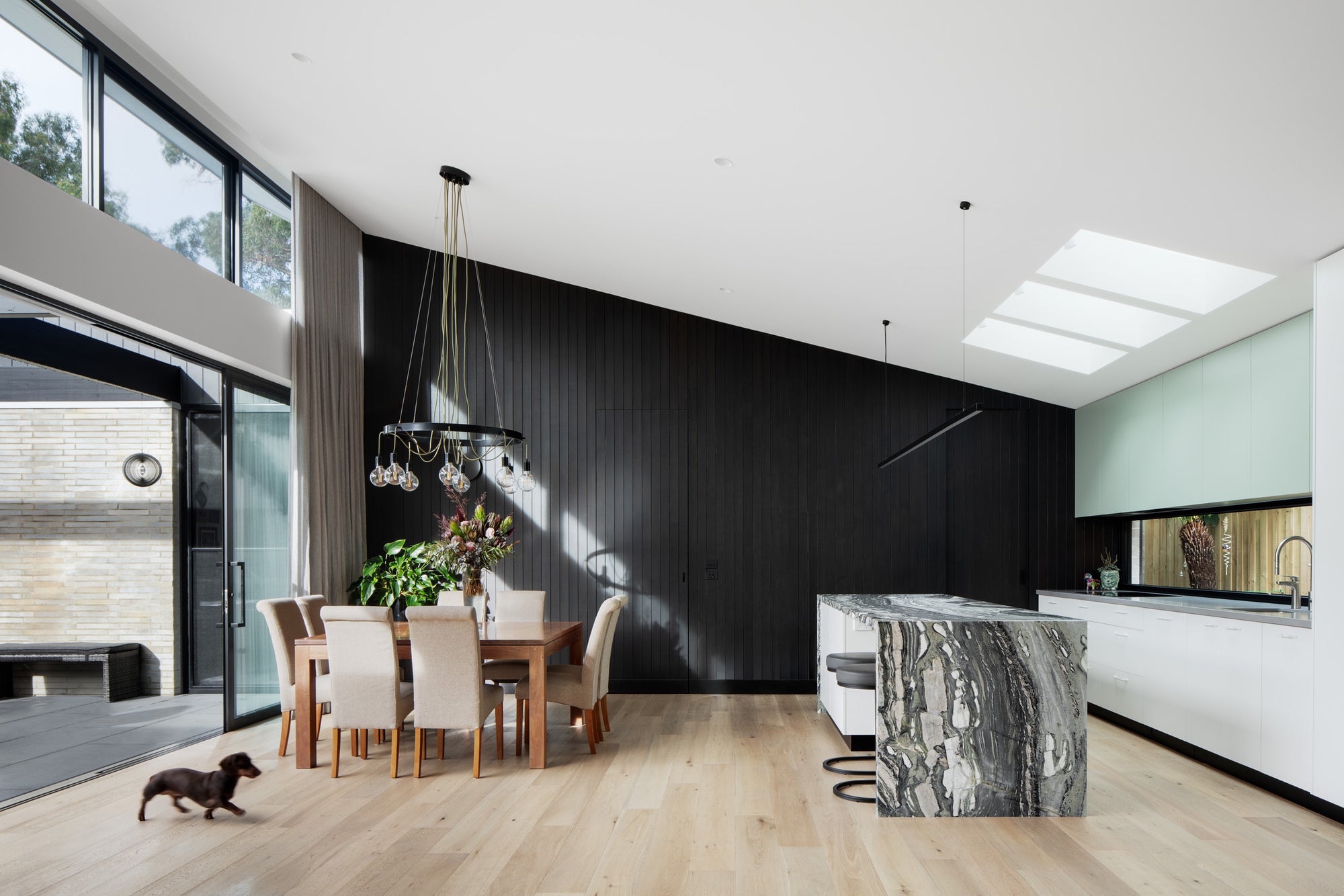 Open-plan kitchen with veined marble island and dark-stained timber feature wall at Campbell St House, Kew