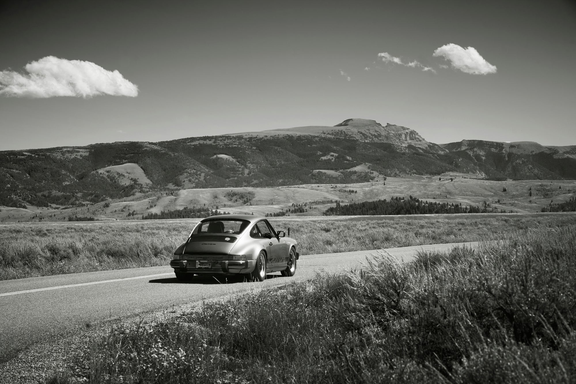 Classic Porsche 911 Carrera driving on a road through scenic Jackson, Wyoming mountains.