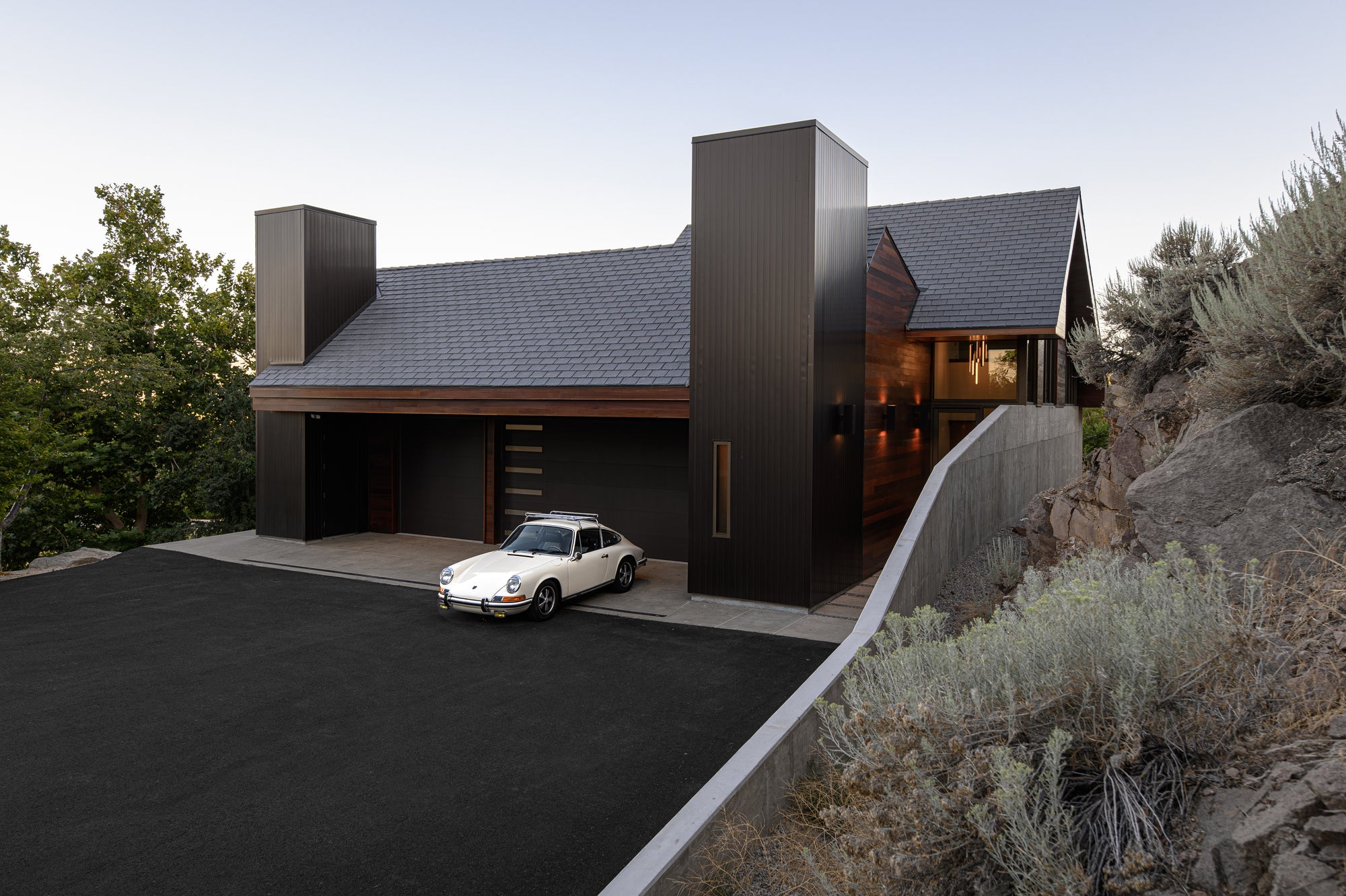 Classic Porsche parked in front of modern garage and home set into natural landscape