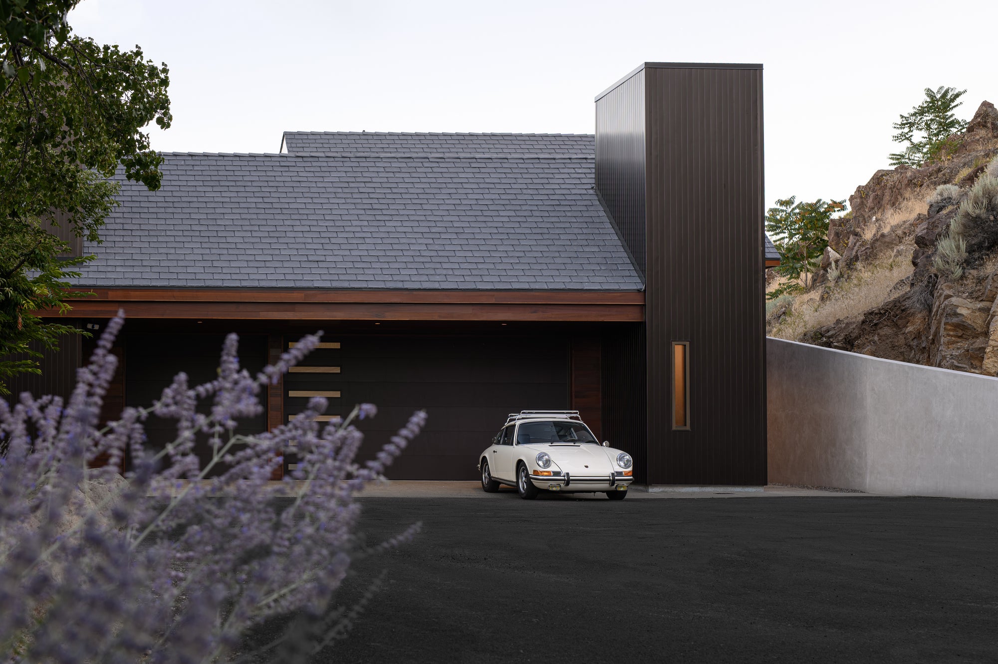 Classic Porsche parked in front of modern garage and home set into hillside landscape