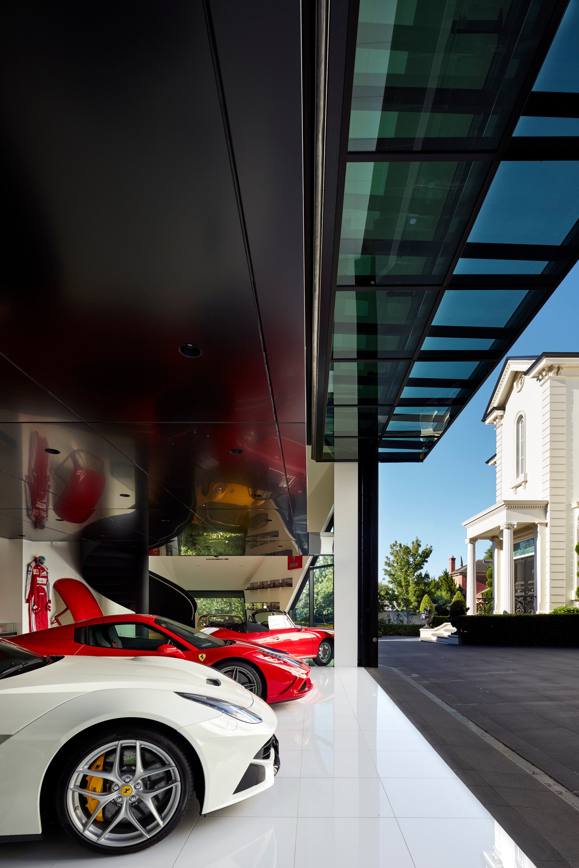 Two Ferrari's, a white and a red one, parked in a modern luxury garage with glass facade.
