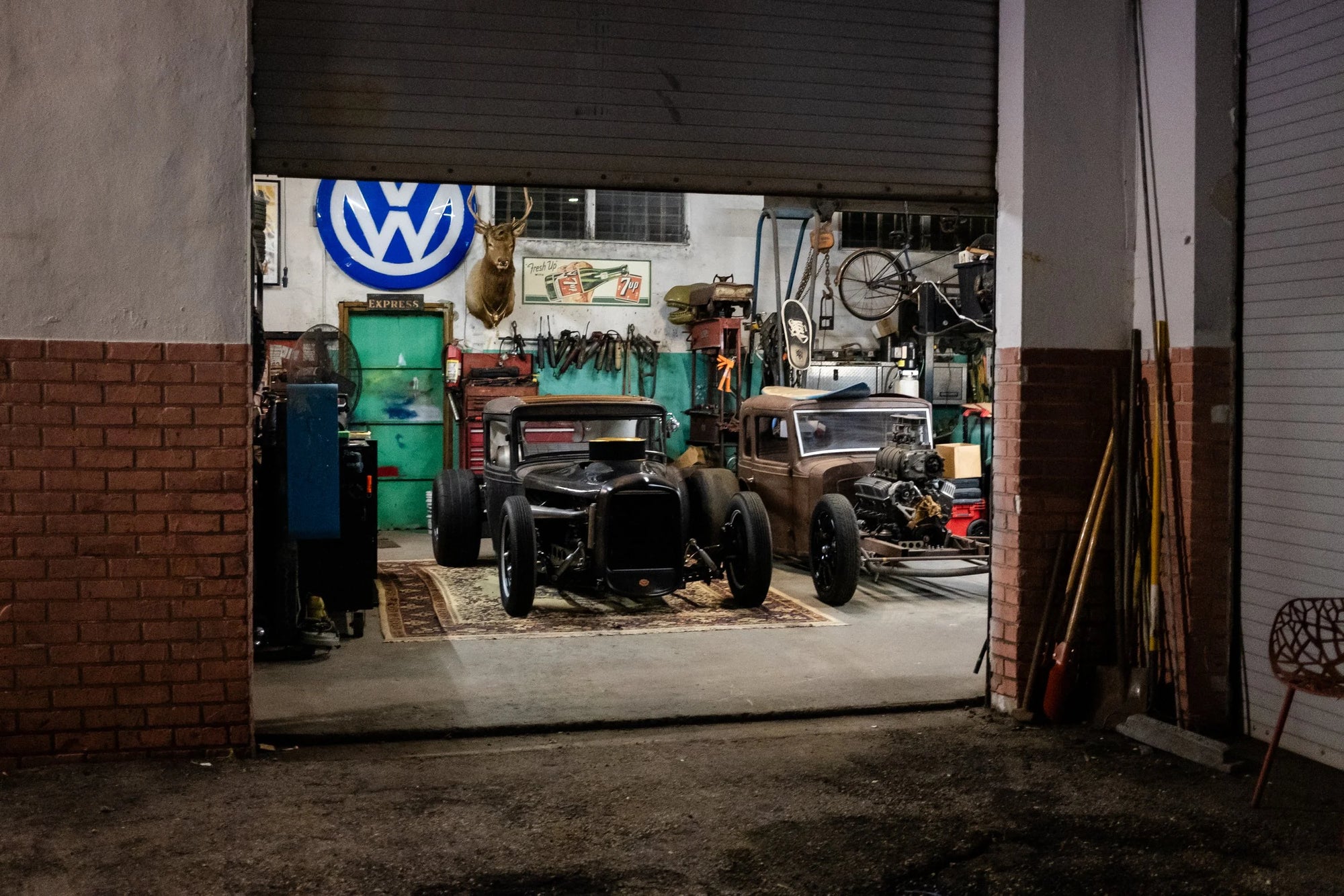 Two custom hot rods parked on a patterned rug in a Ft. Lauderdale garage with vintage decor.