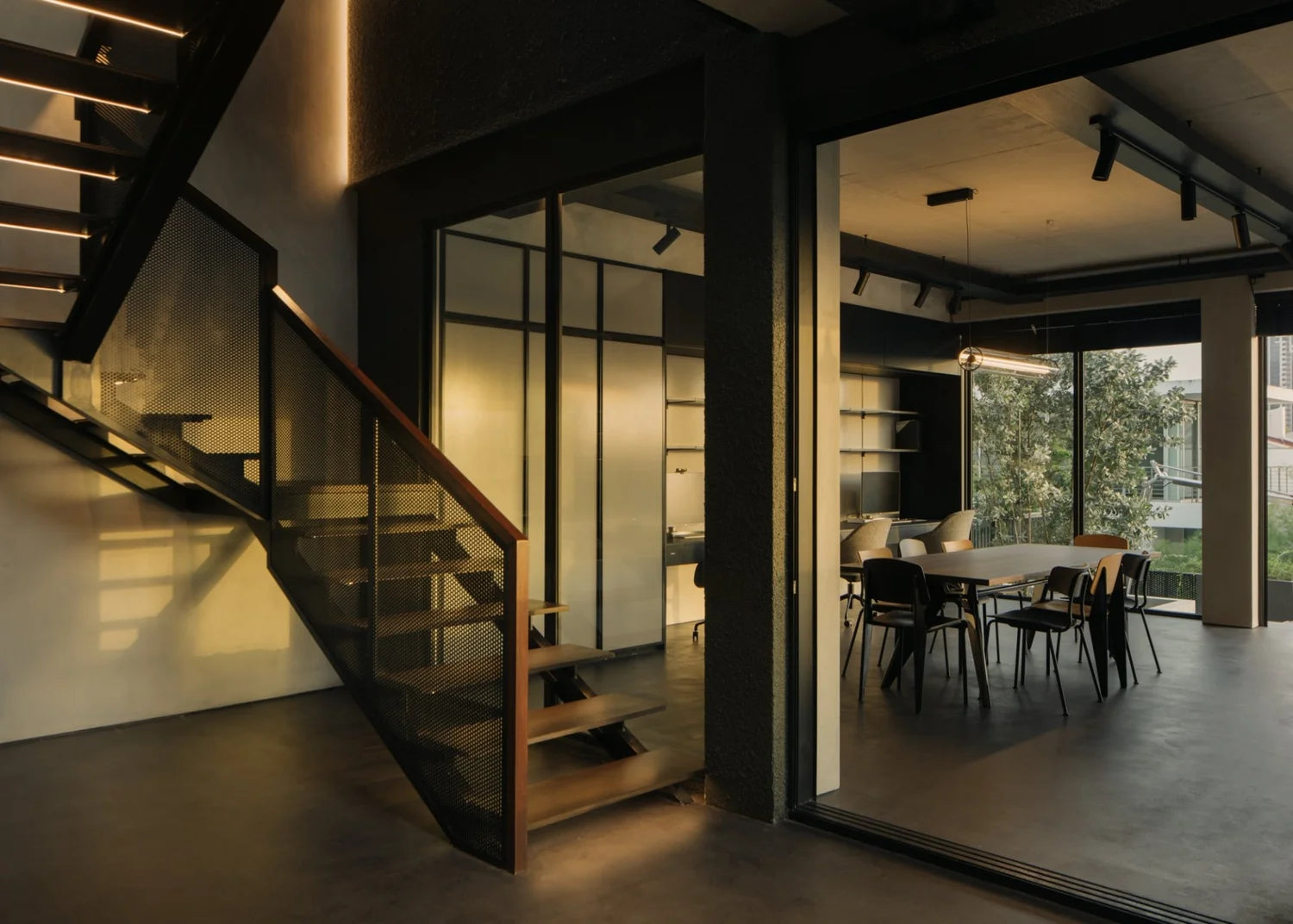 Modern industrial staircase with perforated metal railing and illuminated steps next to a glass-walled meeting room.