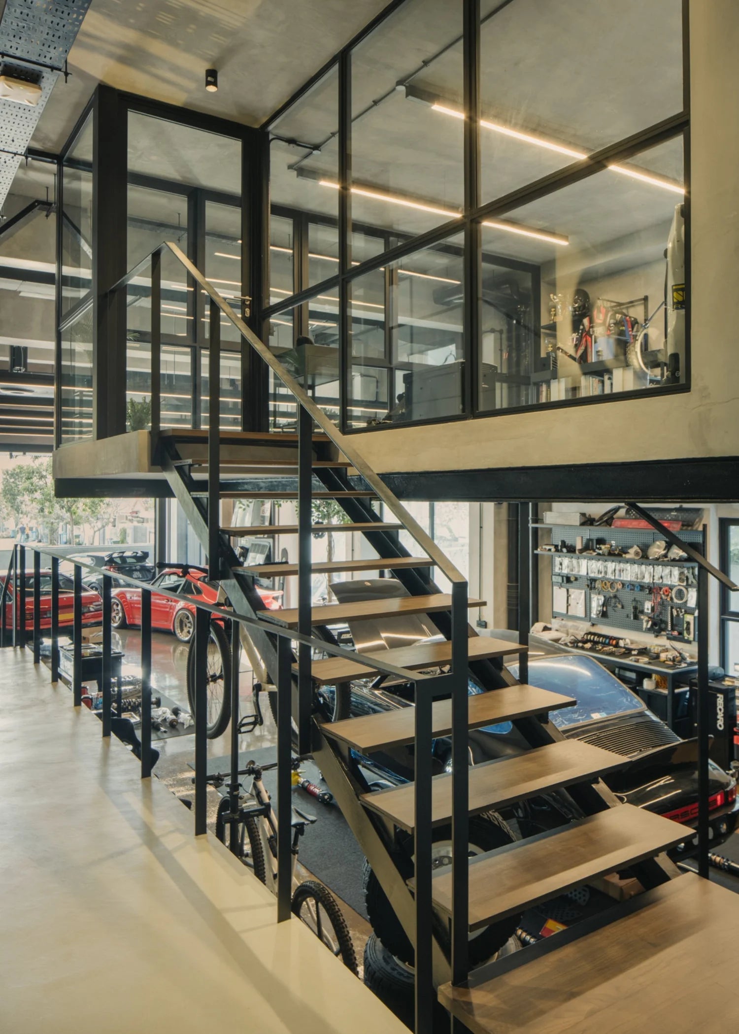 Modern multi-level garage interior with wooden and metal staircase, classic cars, and workshop area.