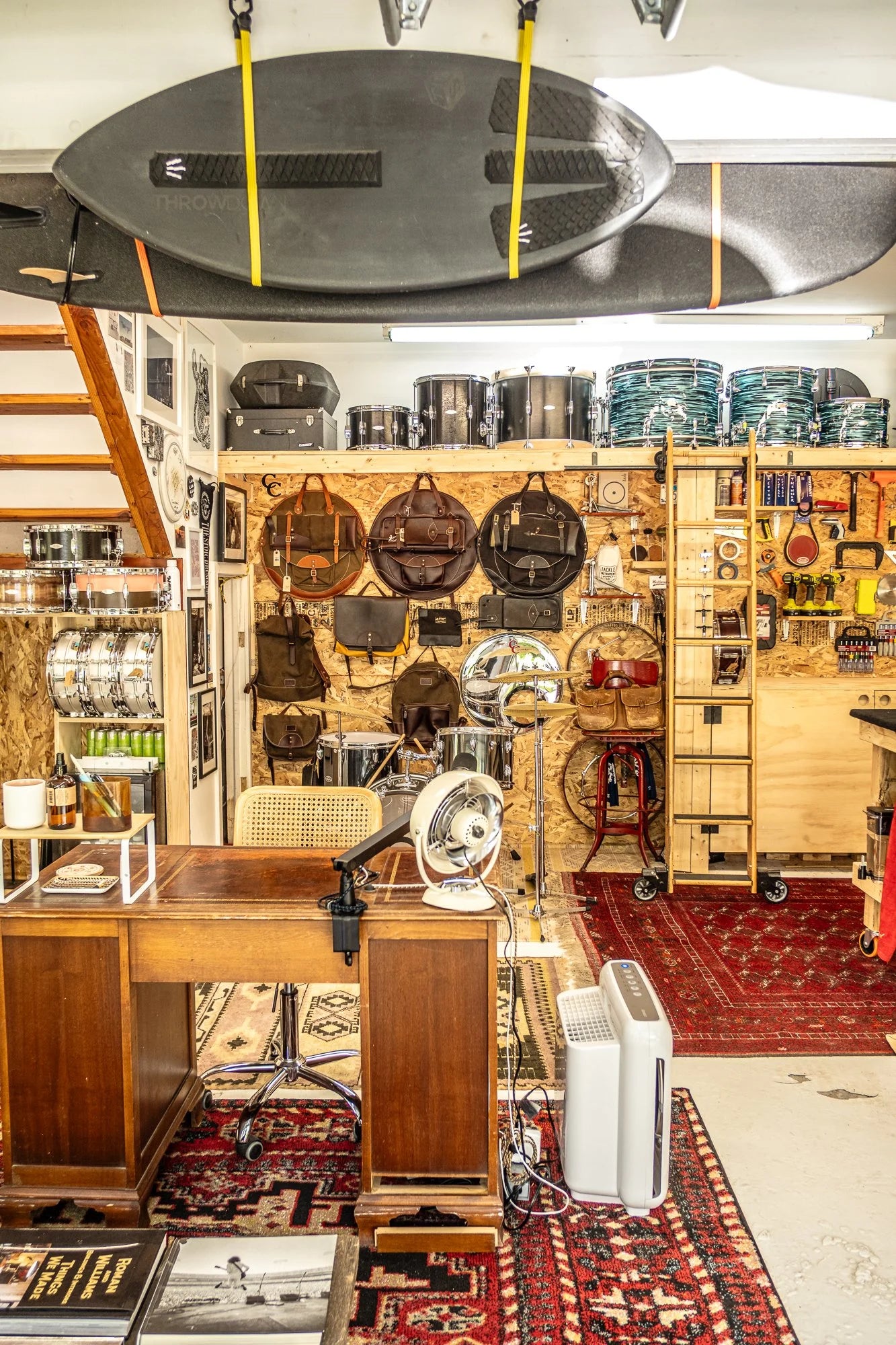 Garage lounge room with shelves, tools, hanging surfboard storage, and equipment on a wooden wall with Persian floor rug.