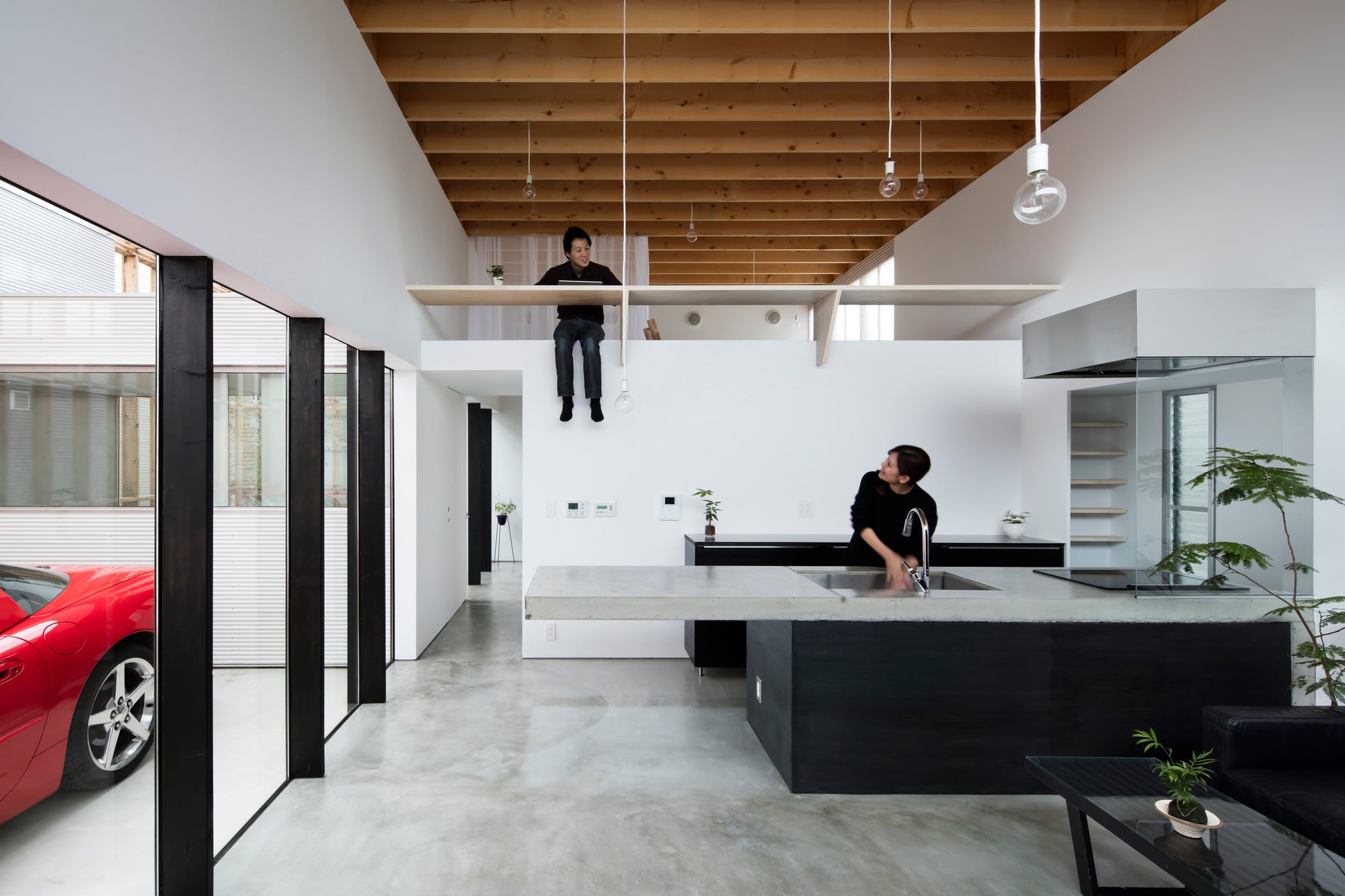 Modern Japanese home interior with red Corvette car in garage visible from kitchen, concrete floors, kitchen, and loft.