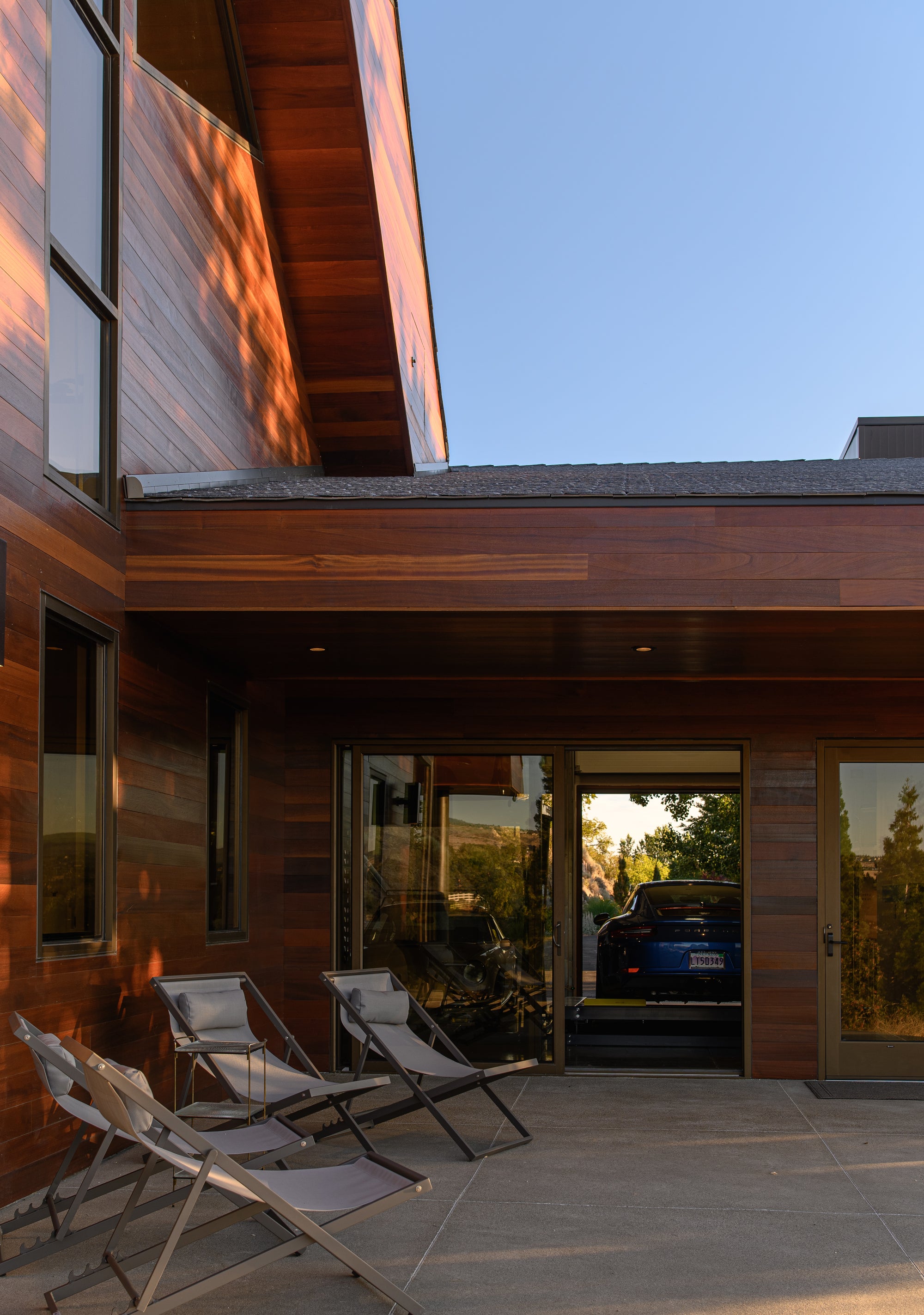 Garage visible from outdoor living space through glass doors with Porsche inside on lift