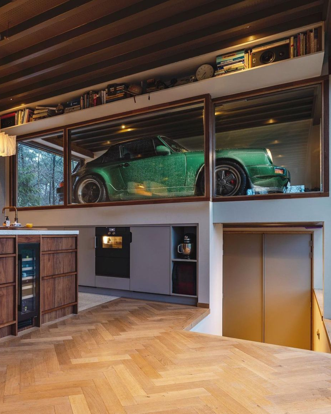 Vintage green Porsche displayed in a glass case garage with views from the kitchen with wooden flooring.