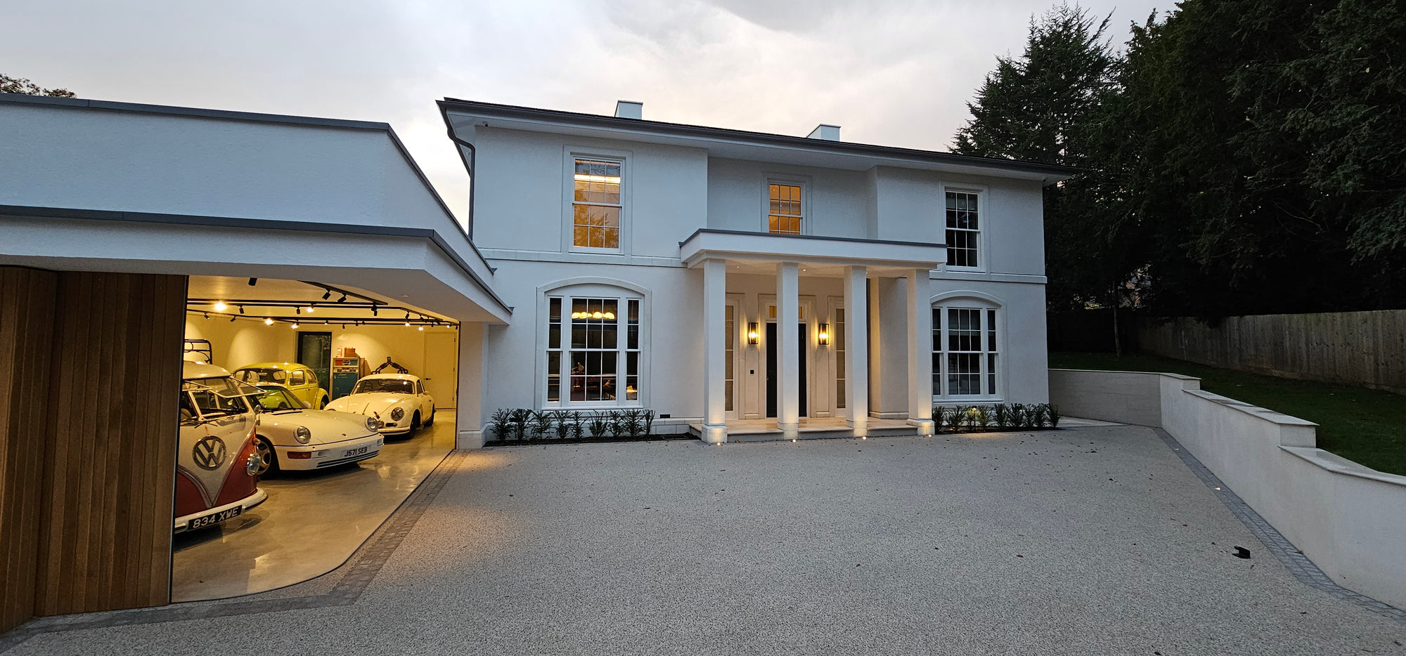 Gulbarg house by NEON Architecture with classic cars in illuminated garage, West Berkshire.