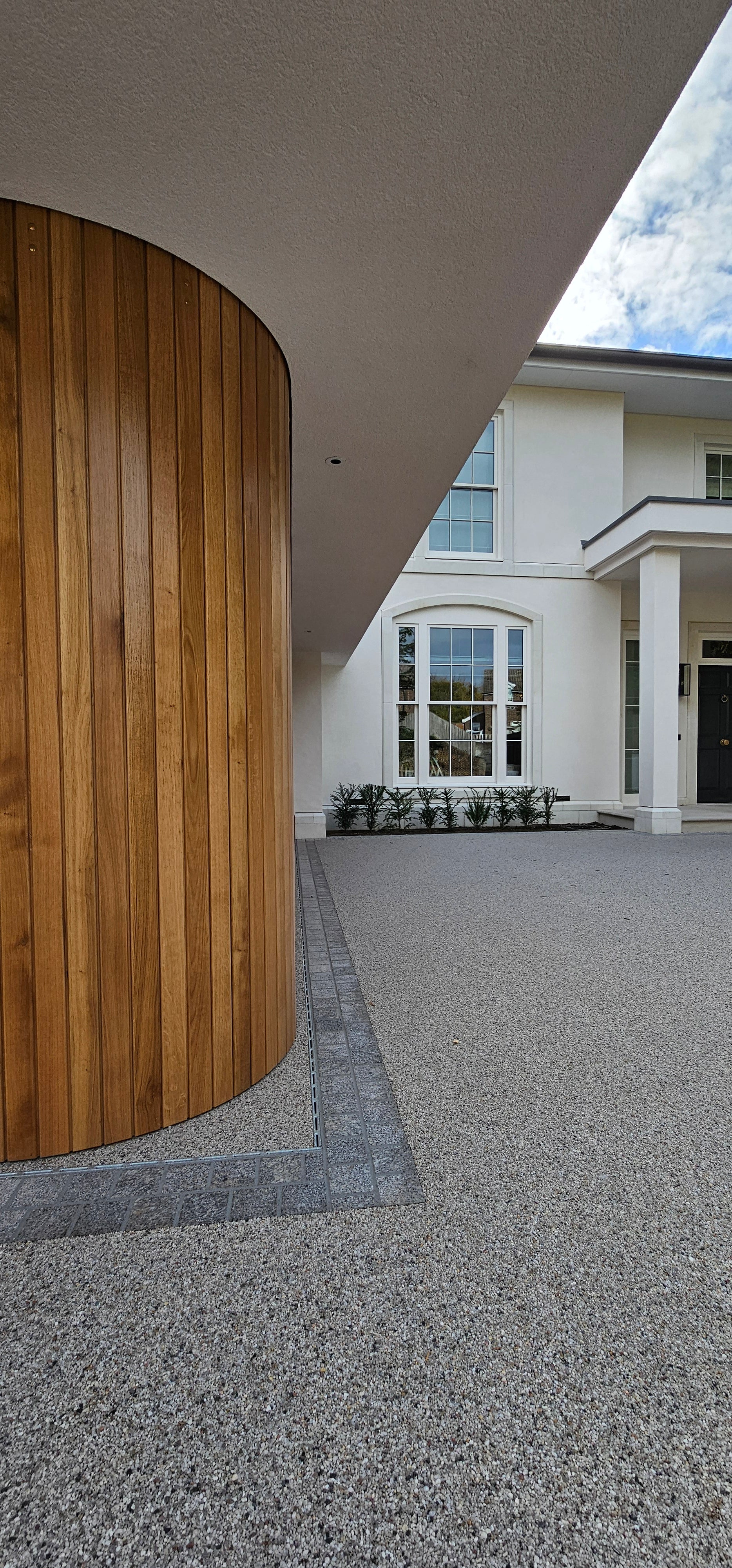 Modern Gulbarg garage with curved oak wood door, exposed aggregate driveway, and white facade.