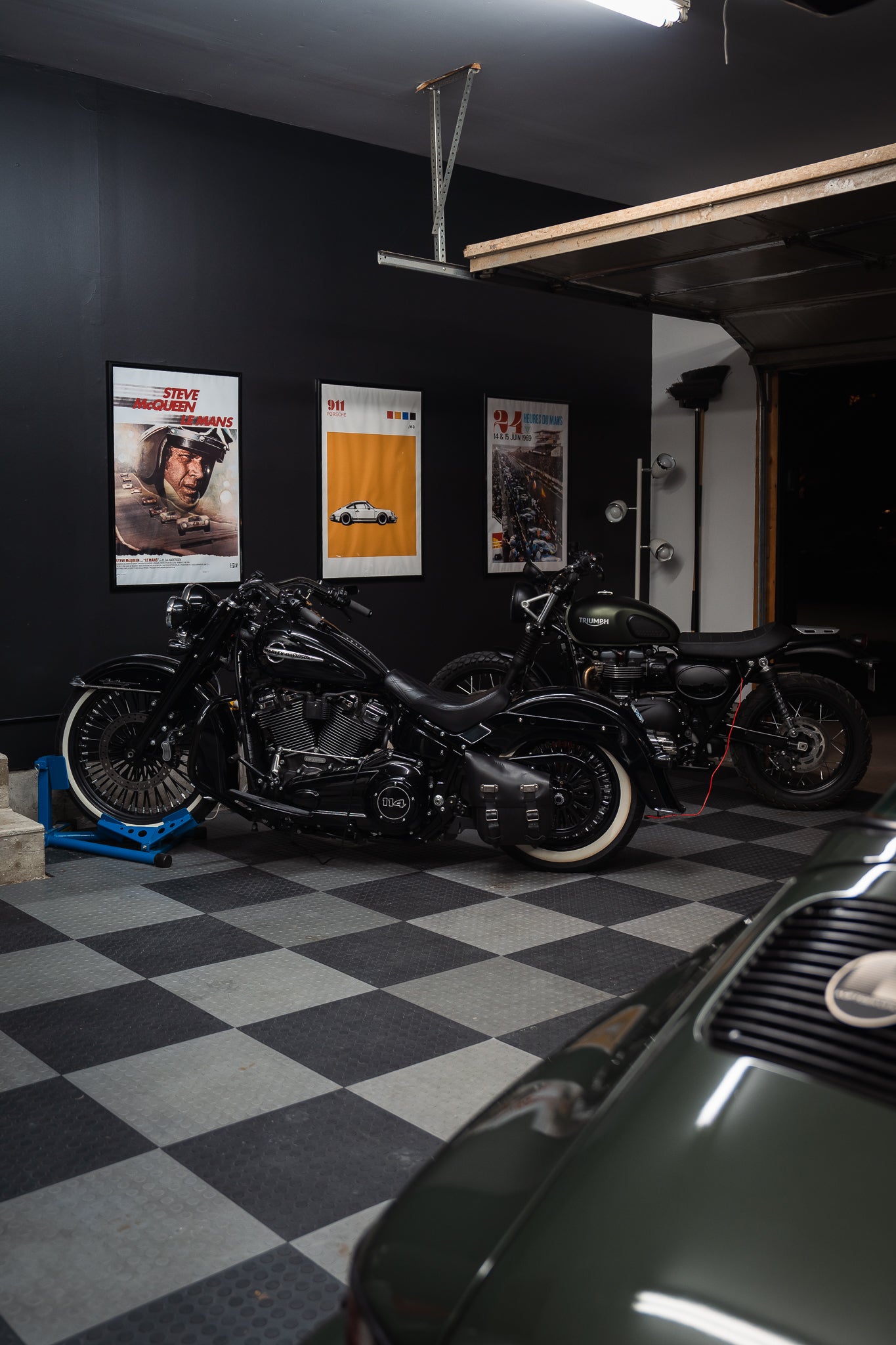 Harley-Davidson and Triumph motorcycles parked inside warm black-walled enthusiast garage