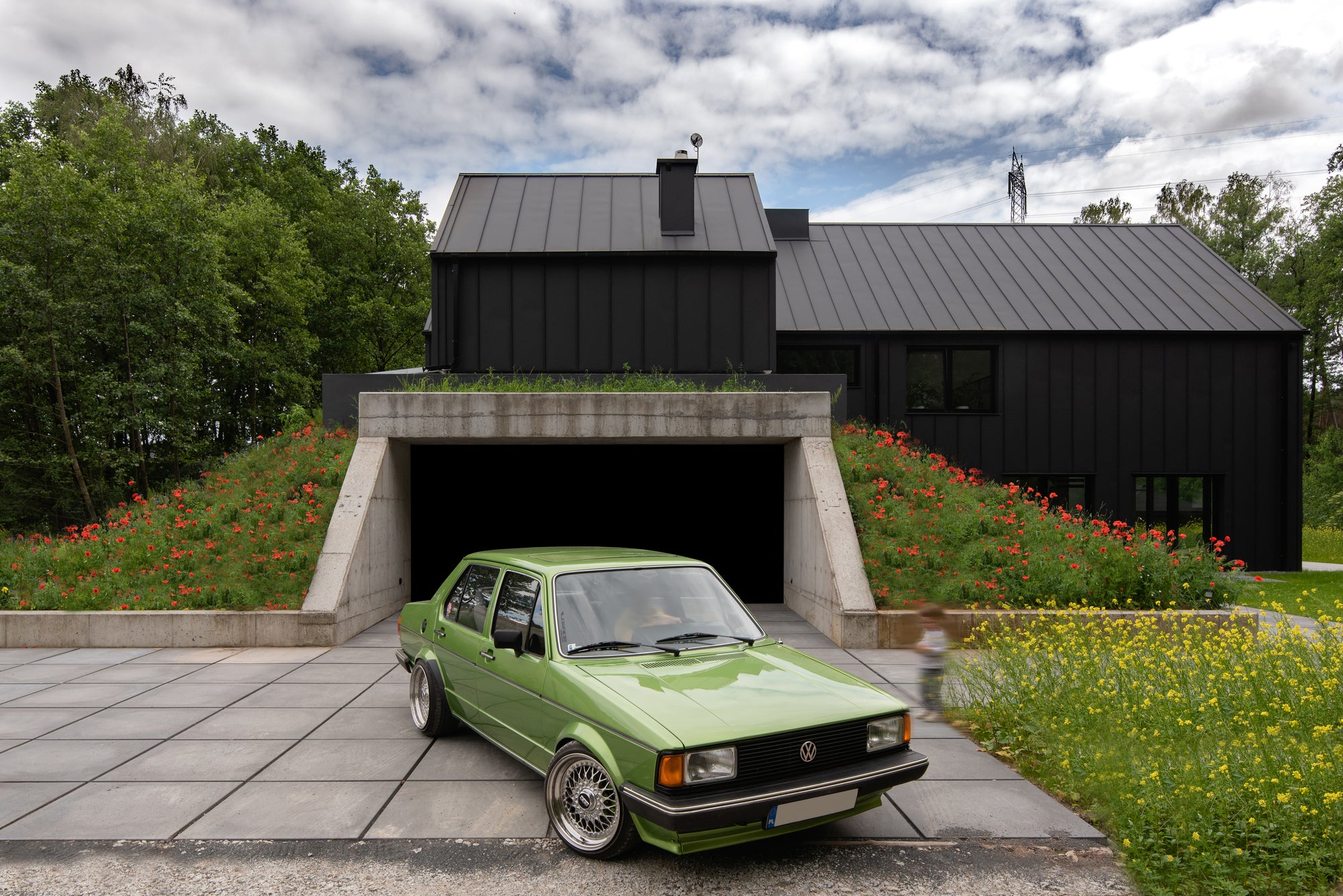 Green Volkswagen Gulf in front of garage integrated into hillside with exposed concrete entry beneath modern home