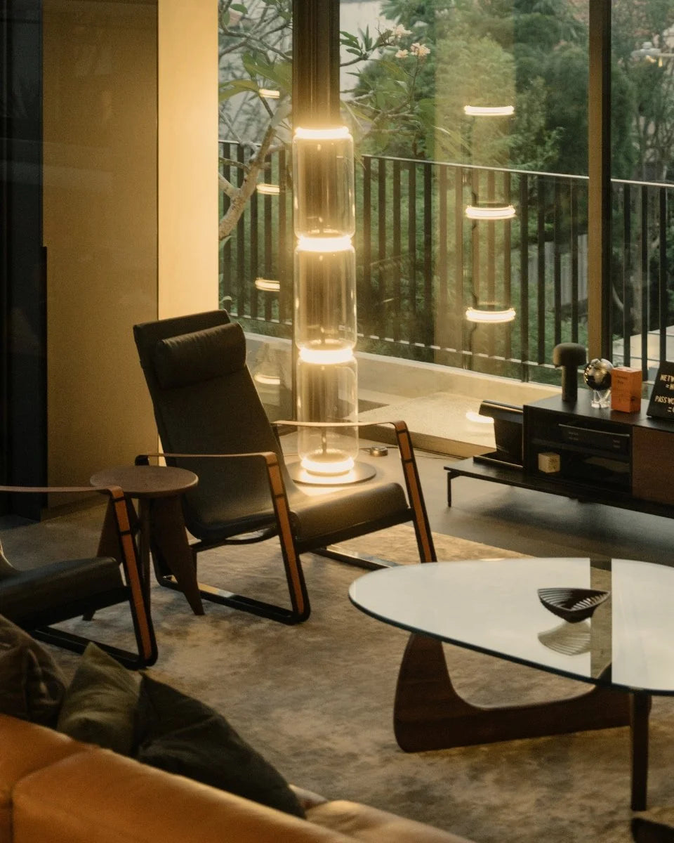 Modern living room with black lounge chair, glass coffee table, and unique vertical floor lamp.