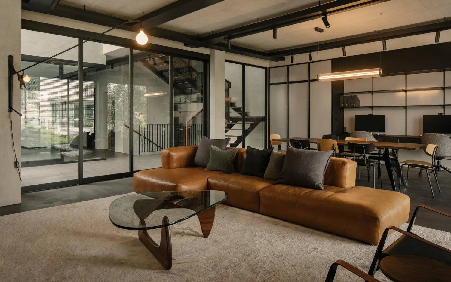 Modern industrial living and dining area with tan leather sectional, glass coffee table, and concrete ceiling.