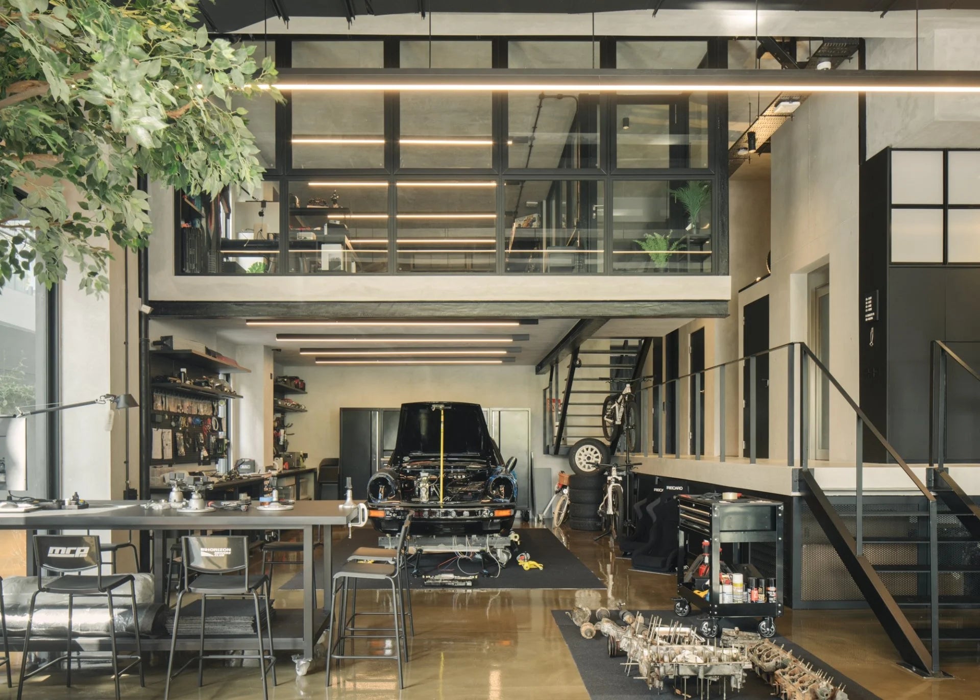 Modern multi-level garage house interior with a classic black Porsche 911 undergoing restoration.