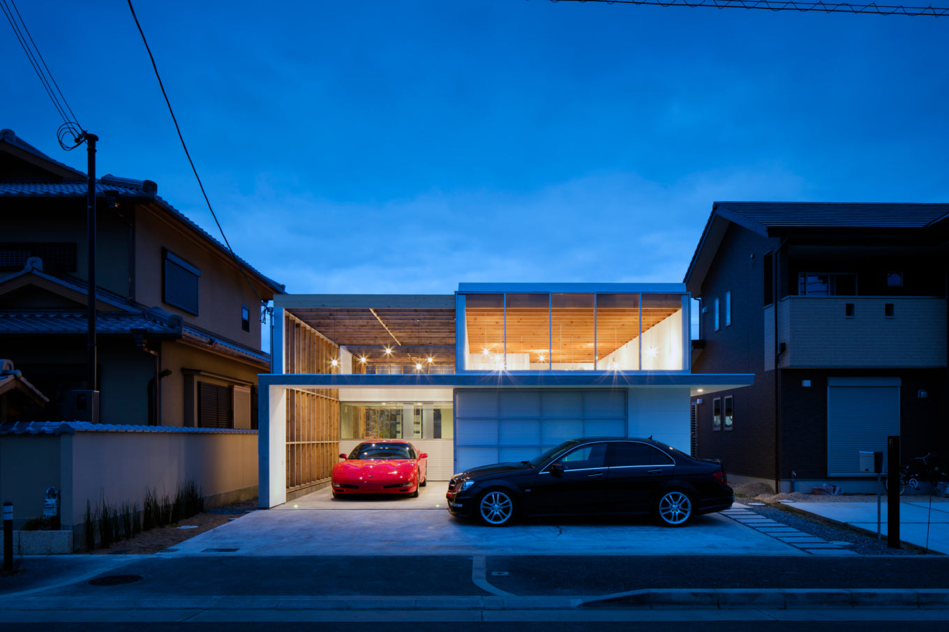 Modern Japanese garage terrace house at dusk with red Corvette and black sedan parked outside.