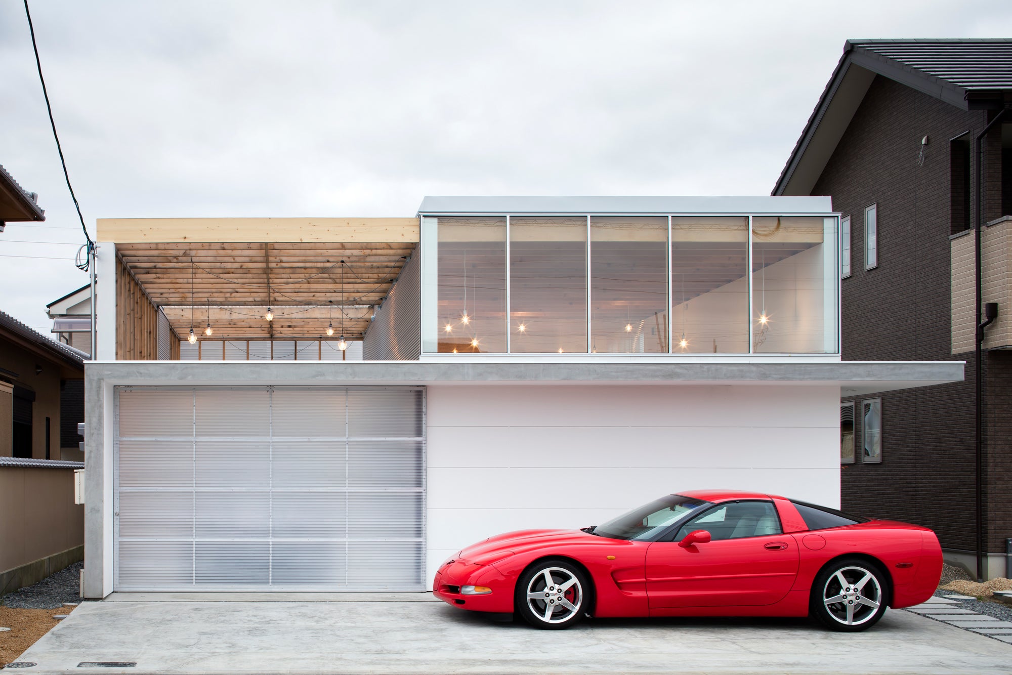 Red Corvette C5 parked in front of a modern Japanese garage terrace house with a wooden pergola.