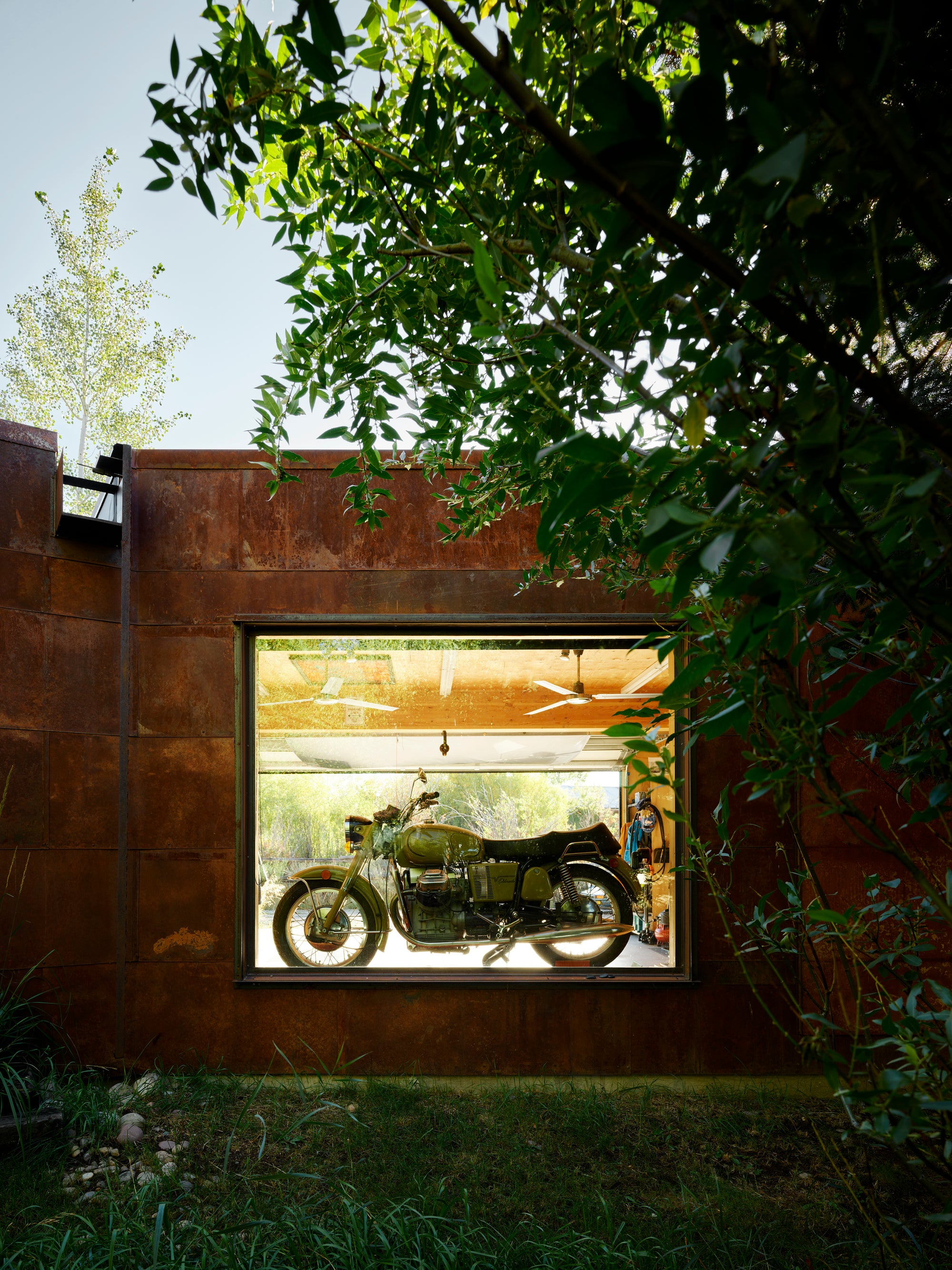 Vintage olive green motorcycle displayed inside a modern Corten steel garage at Logan Pavilion, Jackson, WY.
