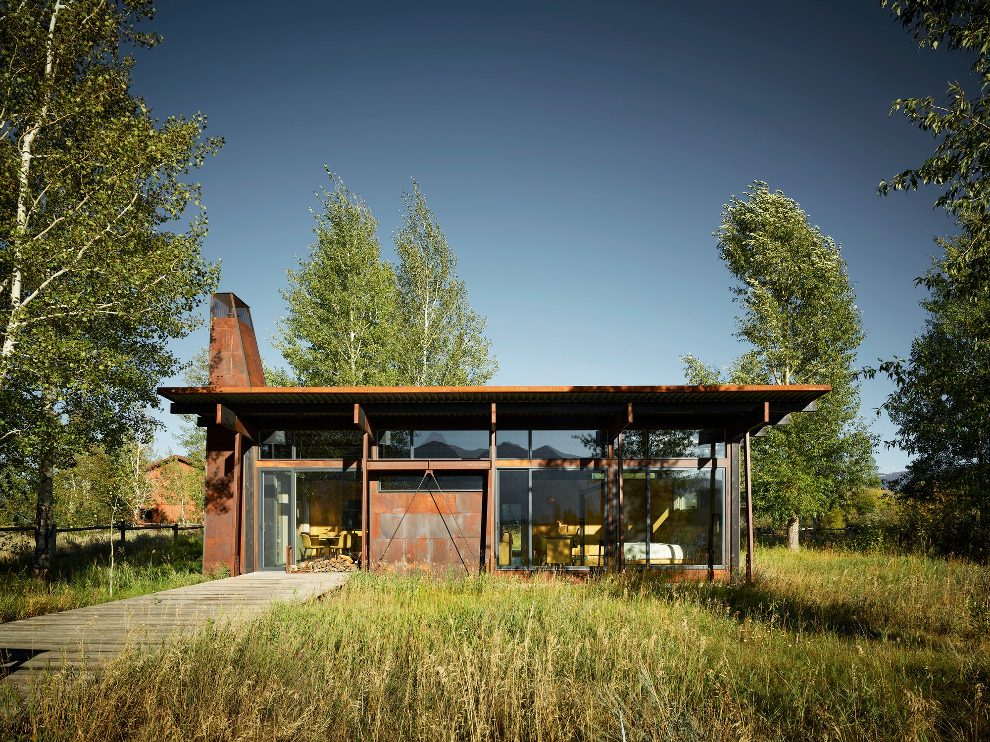Modern corten steel and glass Logan Pavilion house in a grassy field, Jackson, Wyoming.