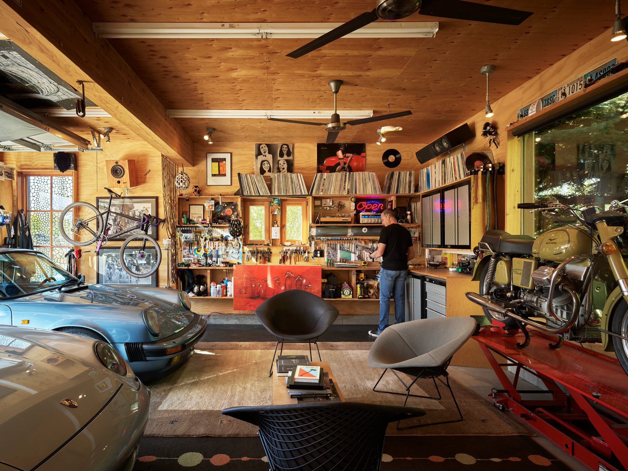 Man in a modern wood-paneled garage with two Porsches, a motorcycle, and records in Jackson, WY.