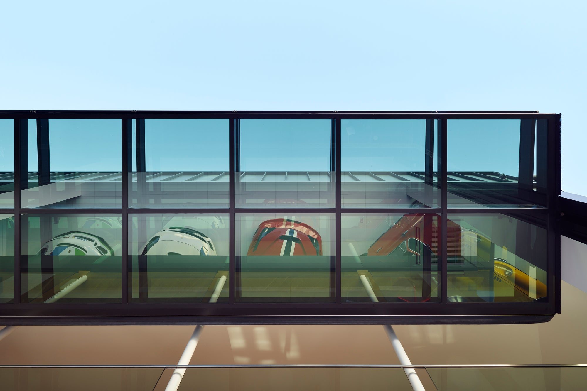 Modern architectural garage structure with glass panels and a clear blue sky with Ferrari and Porsche cars