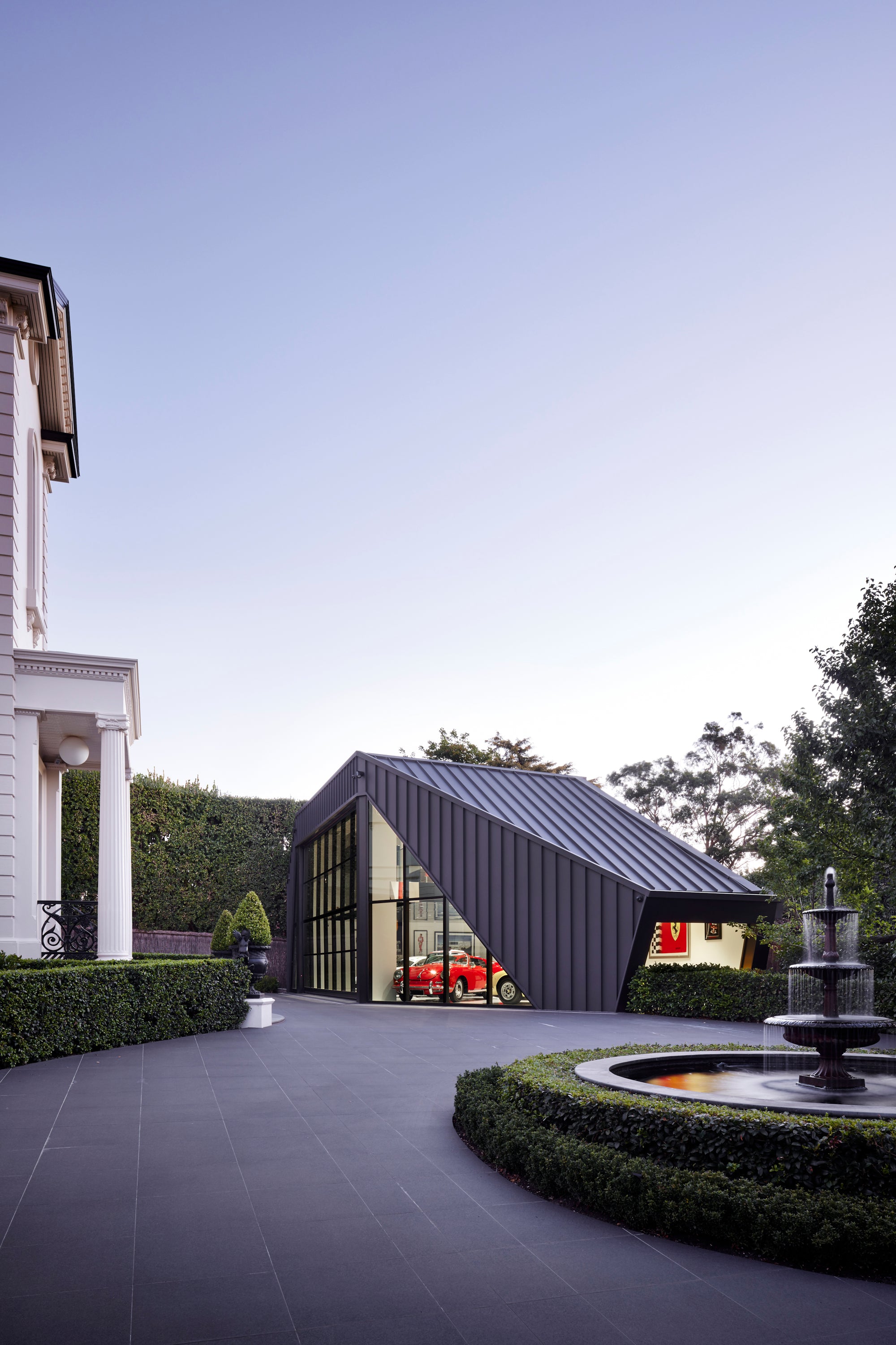 Modern luxury supercar garage with a driveway and fountain in a well-maintained garden.