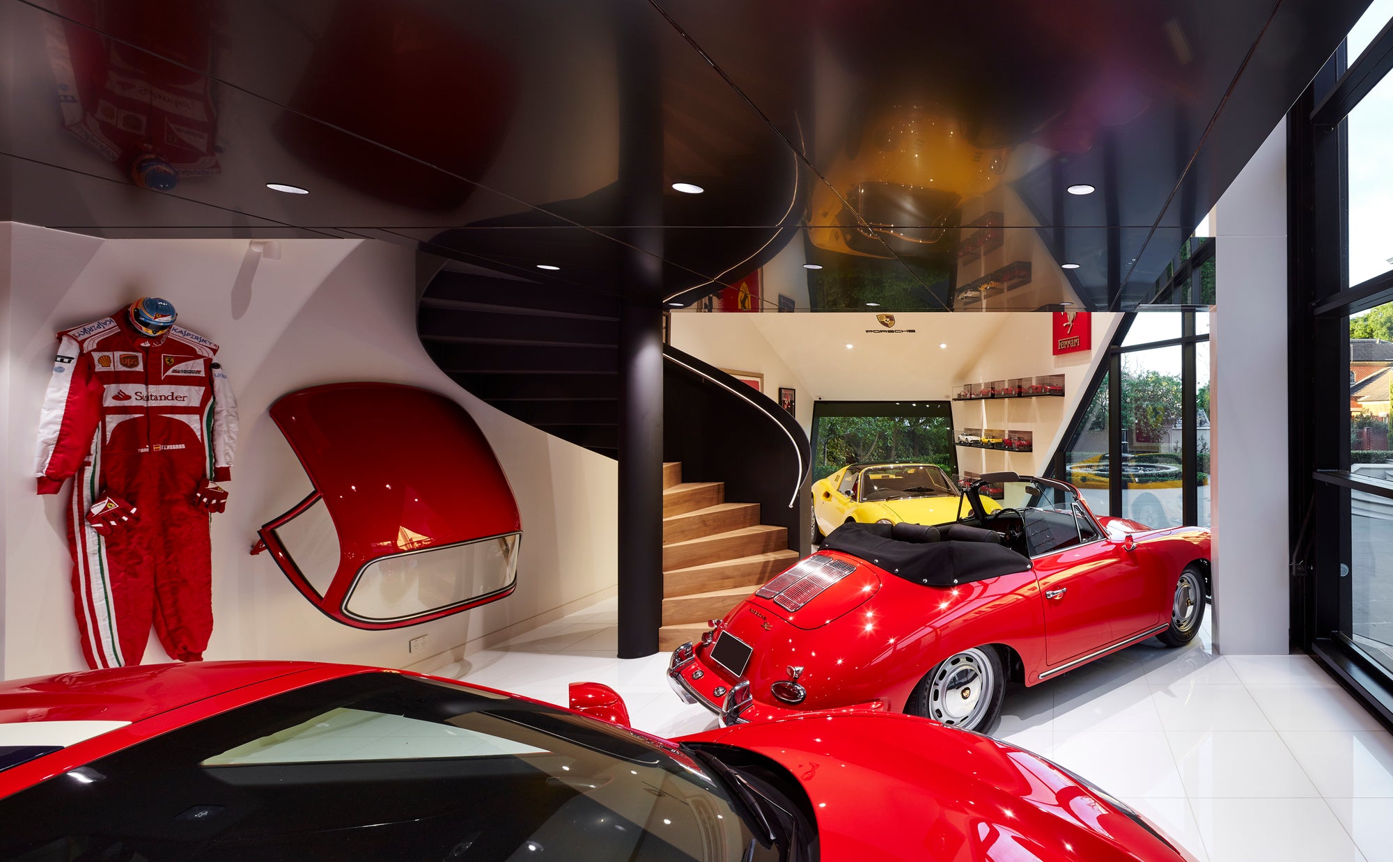Red Ferrari and Porsche in a luxury garage interior with a spiral staircase and wall memorabilia display.