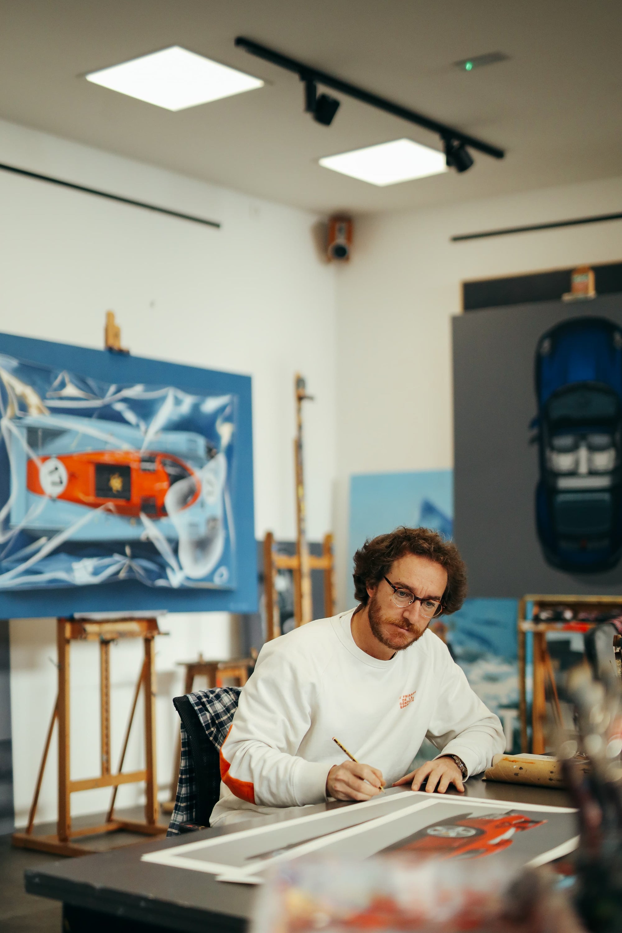 Manu Campa working on a painting in an art studio and garage with various automotive artworks around.