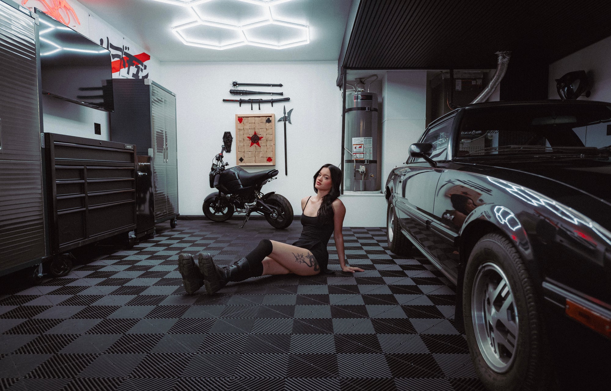 Black Mazda RX-7 parked inside a JDM-themed garage in Las Vegas with hexagonal LED ceiling lights and checkerboard floor