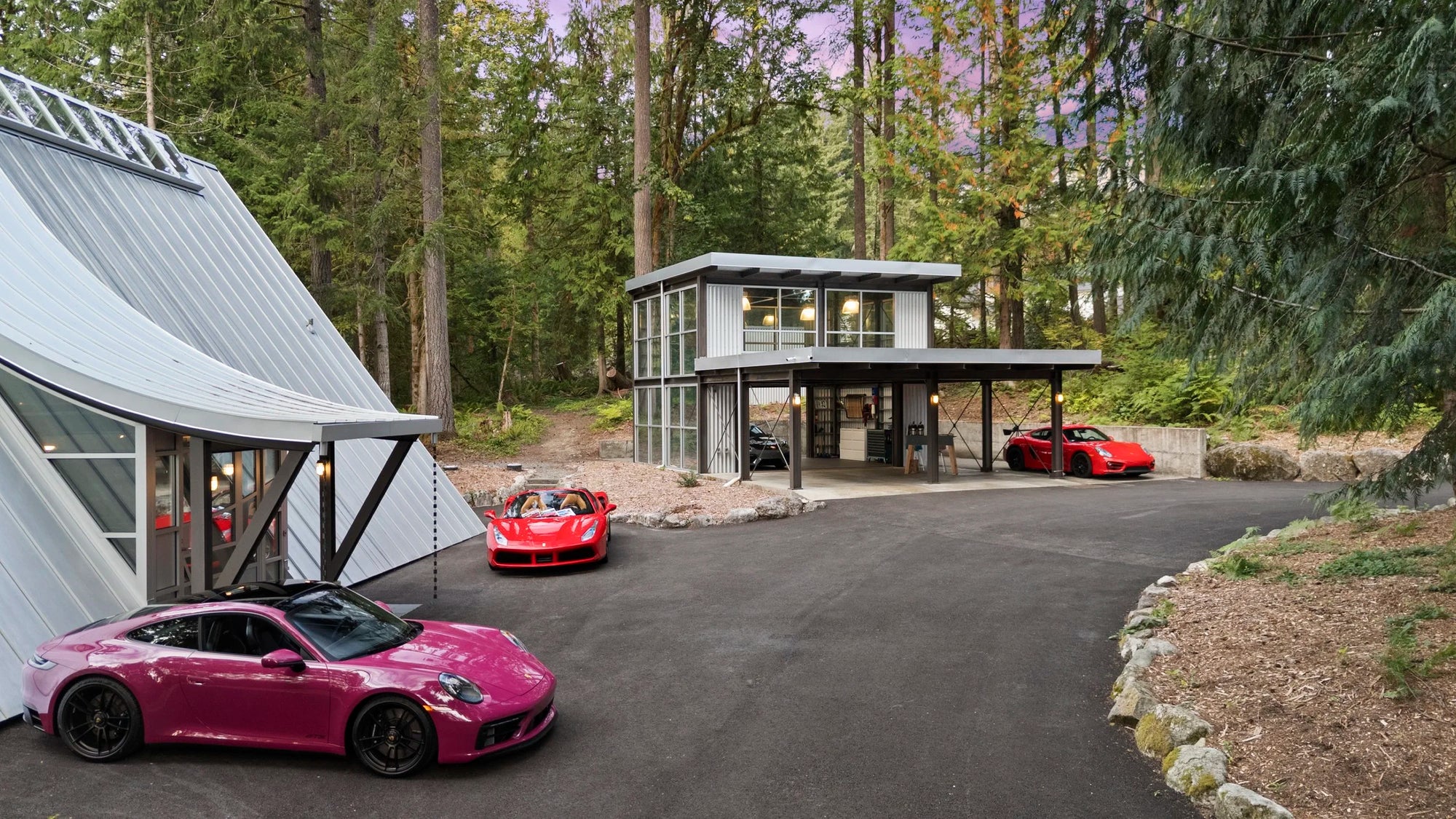Modern A-frame house and detached glass and steel garage workshop with a driveway featuring two Porsche and one Ferrari. 
