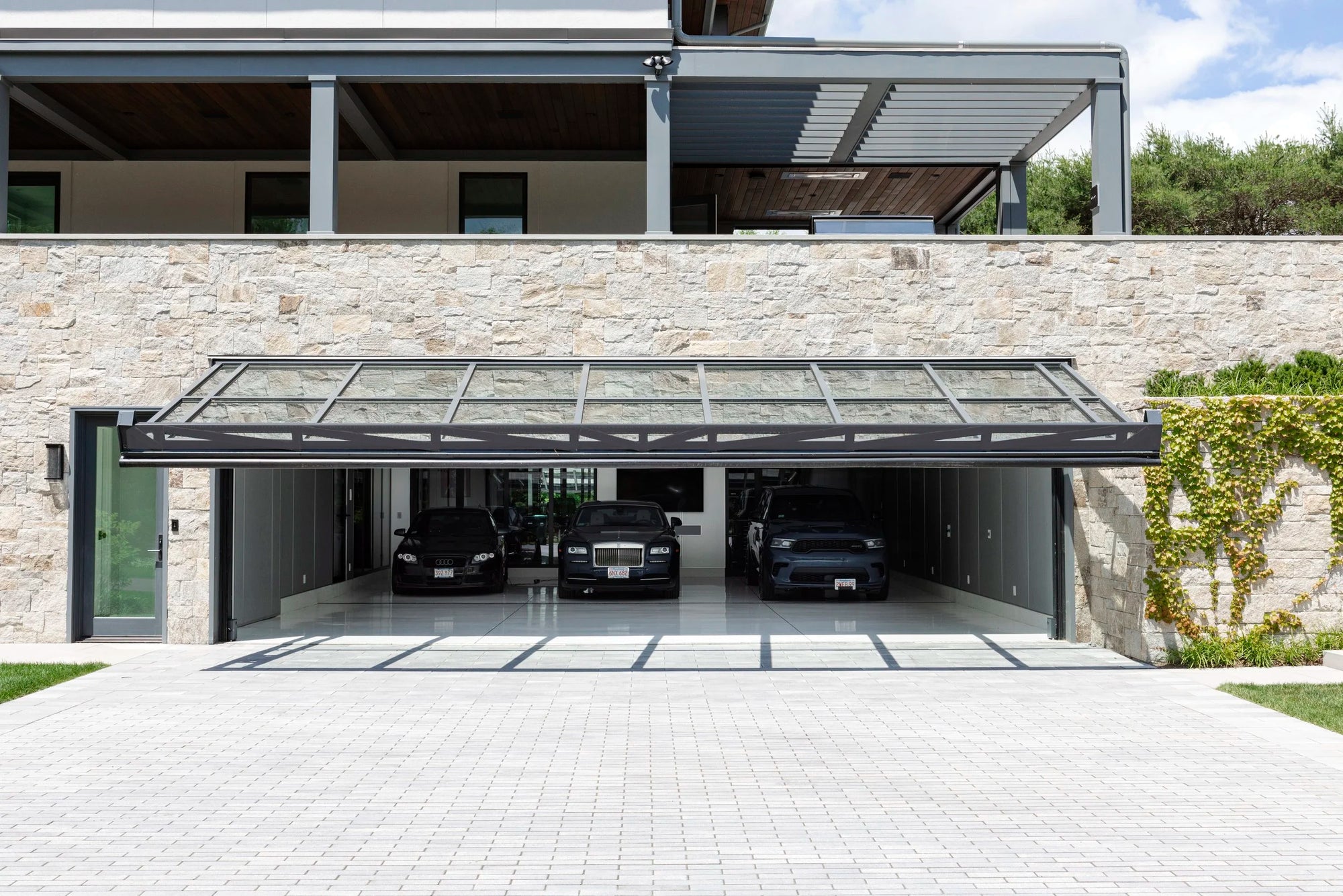 Modern house with a glass door garage and parked car collection underneath. 