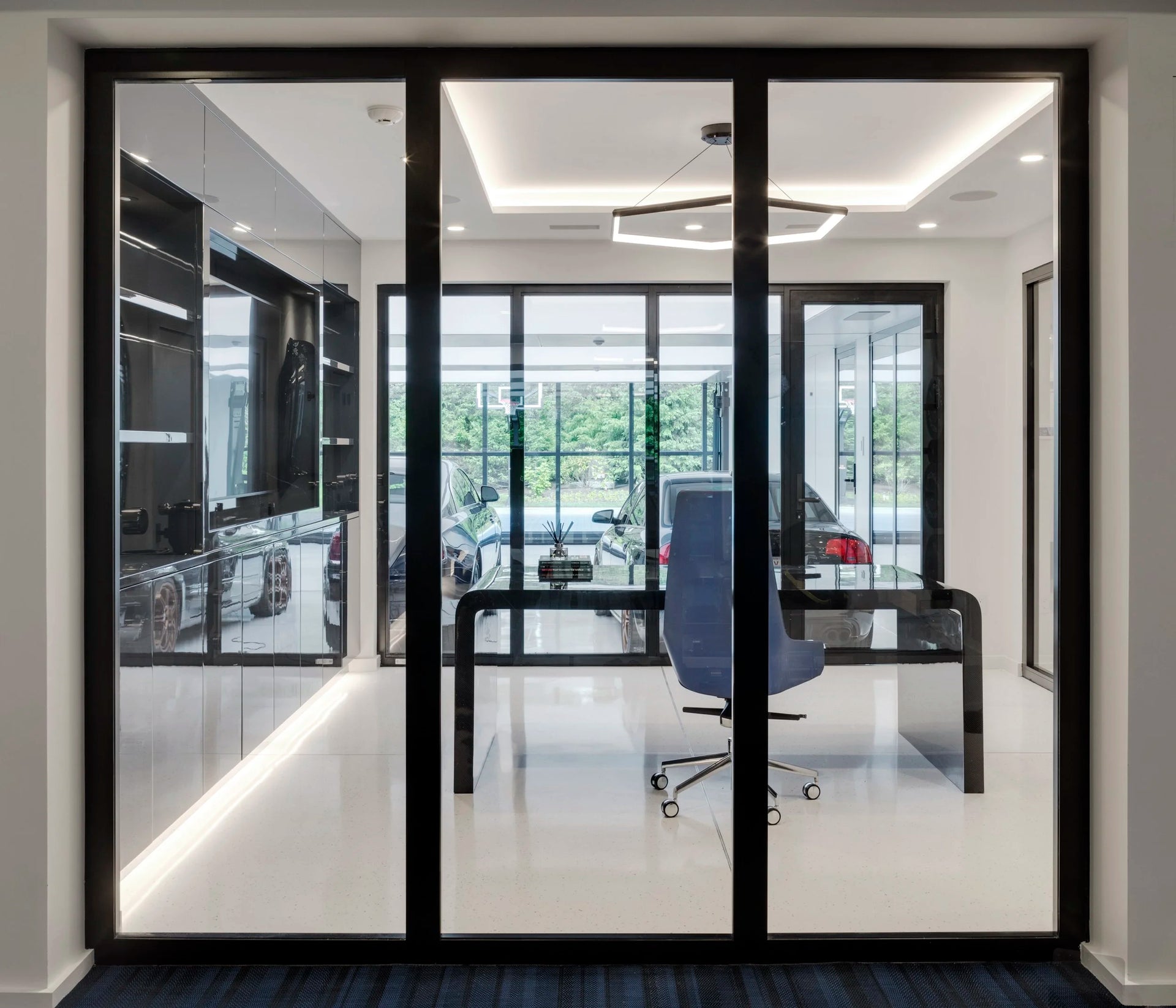 Modern office interior with desk and glass wall views to car collection located in garage. 