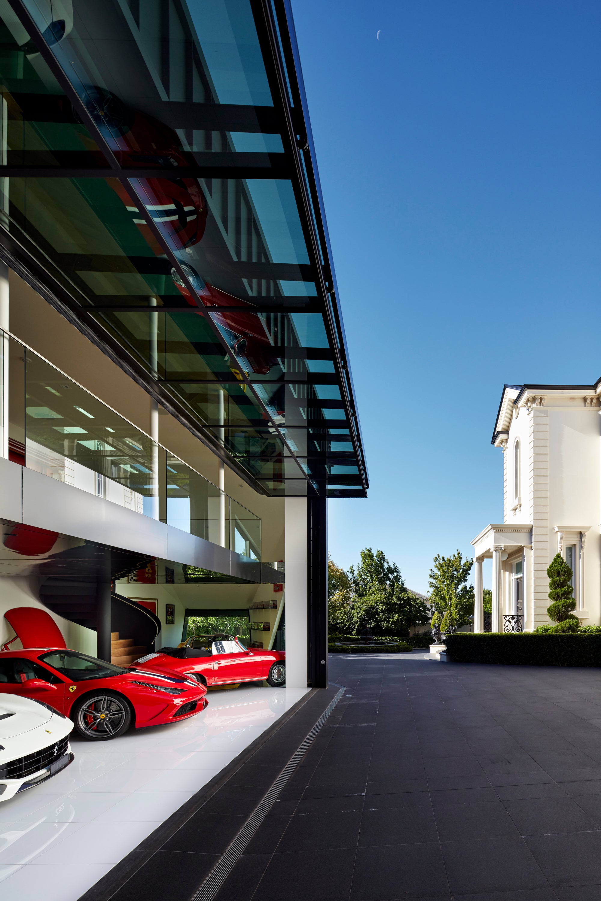 Modern supercar showroom garage with red Ferrari, white Ferrari, and red Porsche on a clear day.