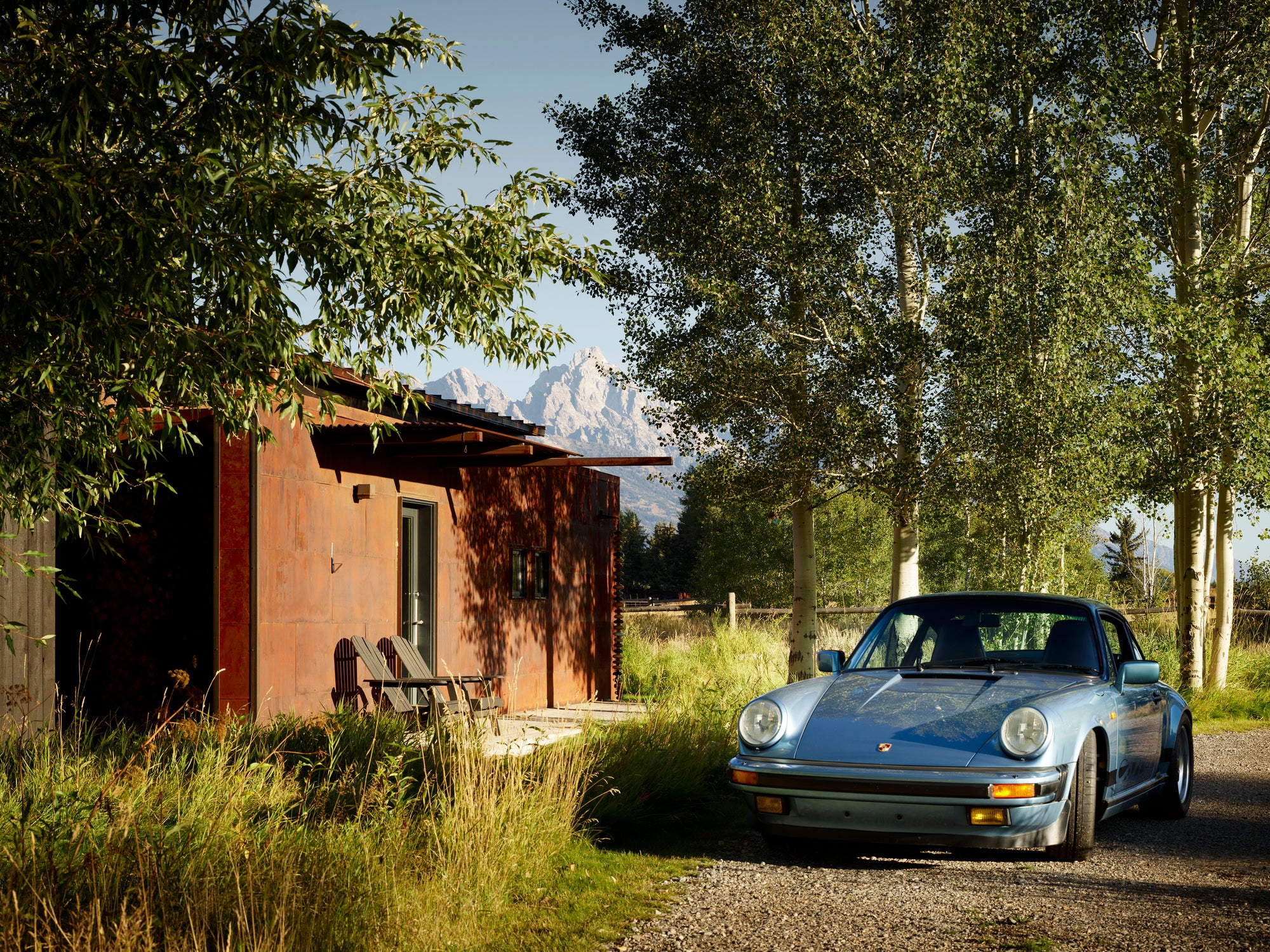 Light blue classic Porsche 911 parked beside a Corten steel cabin with Teton mountains in Jackson, Wyoming.