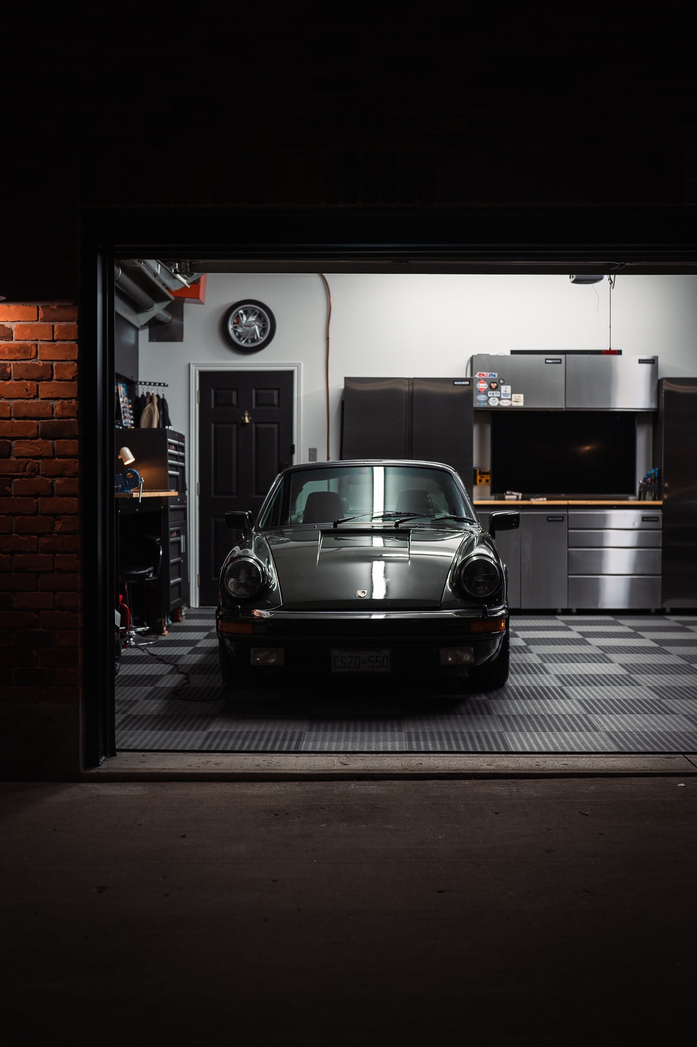 Front view of a 1977 Porsche 911 parked inside illuminated home garage at night