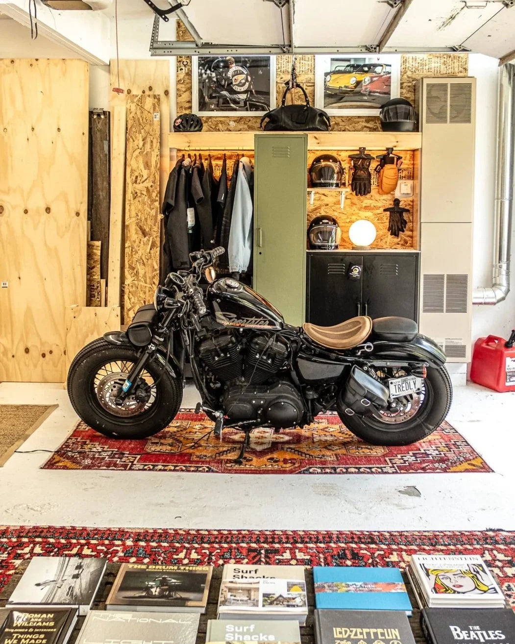 Spacious Hudson Valley garage workshop with Harley Davidson motorcycle, drums, tools, eclectic wall art, and floor rugs. 