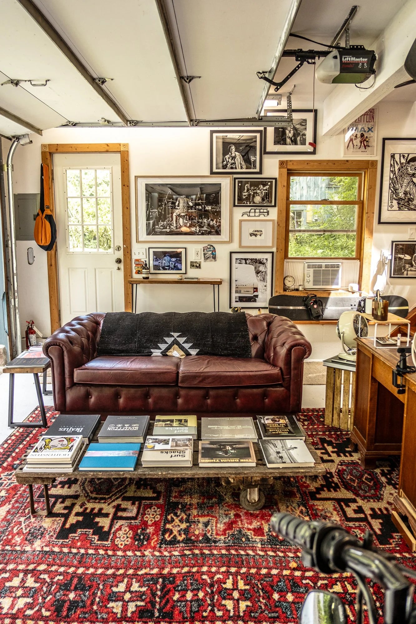 Cozy converted garage living space in Hudson Valley with a brown leather Chesterfield sofa, patterned rug, and music-themed wall art.