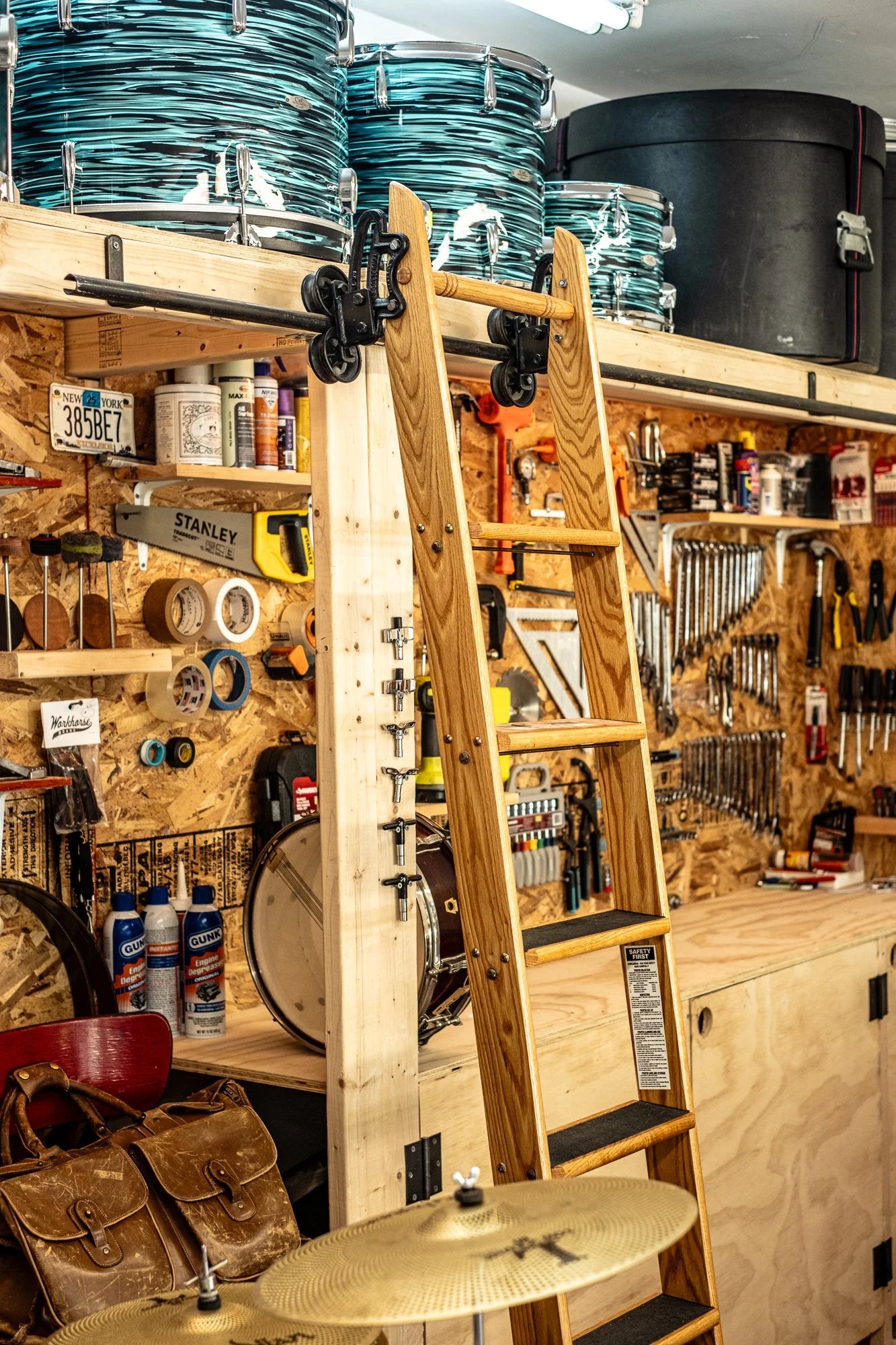Rolling wooden library ladder in a well-organized garage workshop with tools and drum kits.