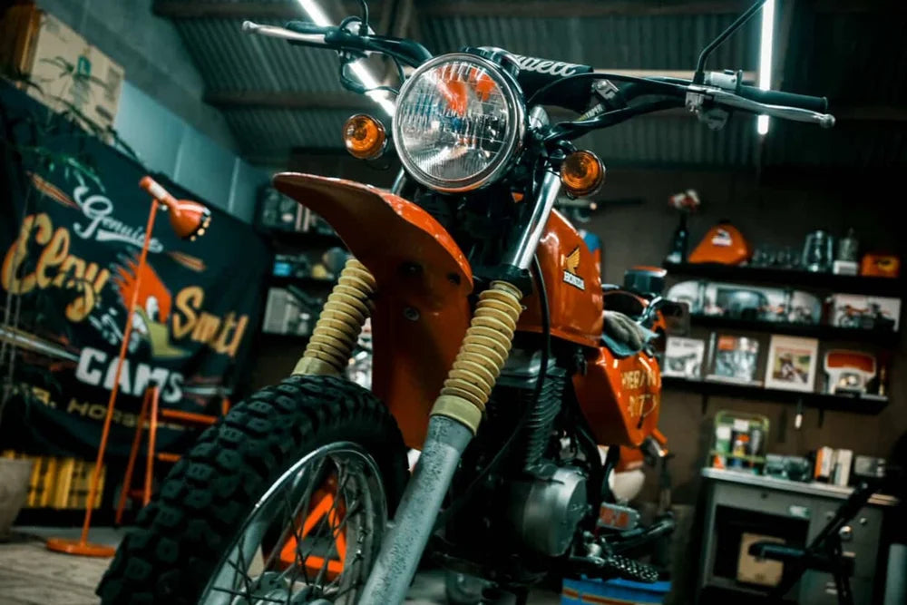 Close-up of a vintage Honda motorcycle in a garage setting with various items in the background.