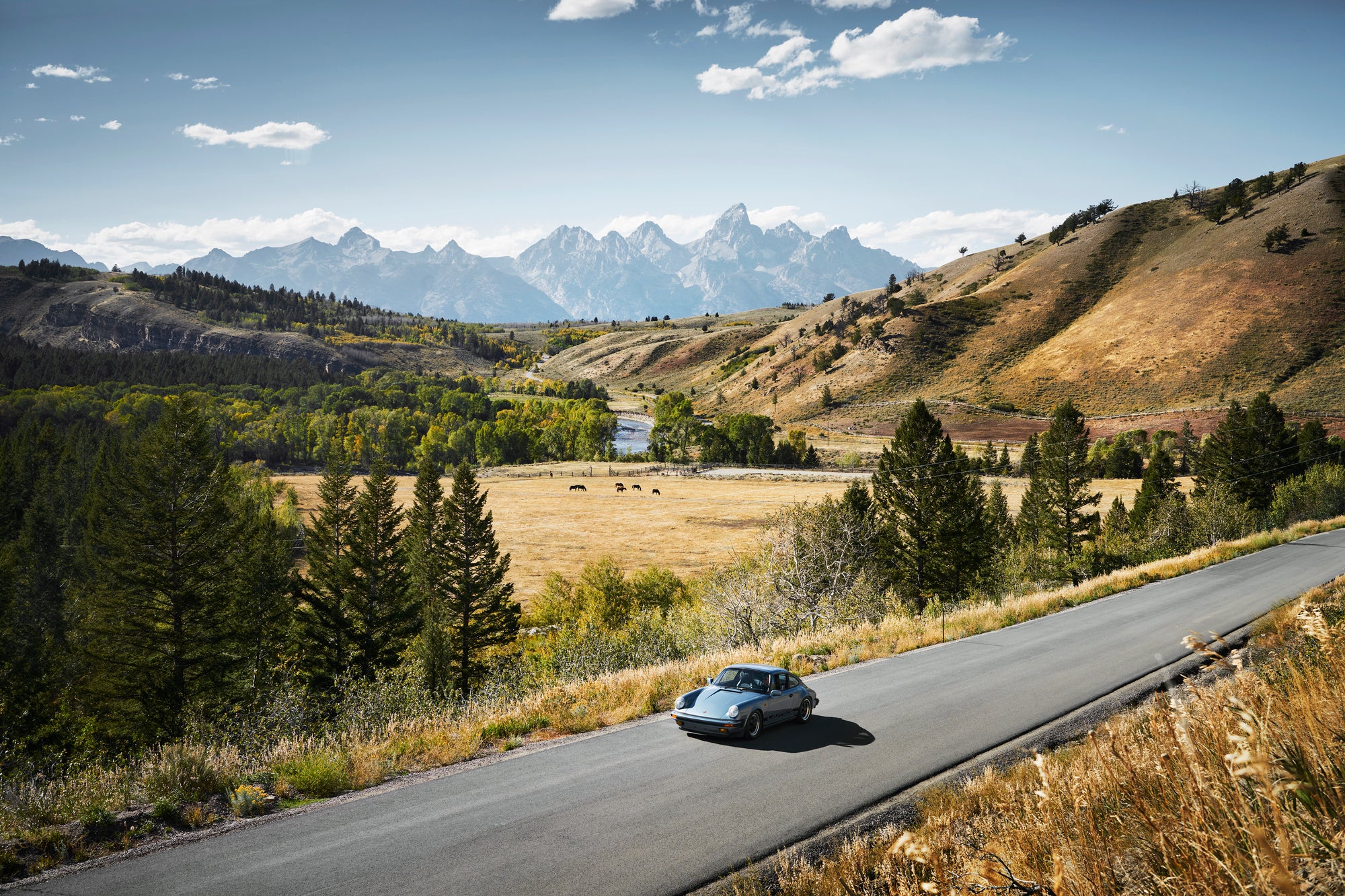 Light blue vintage Porsche 911 driving on a scenic road with Grand Teton mountains.
