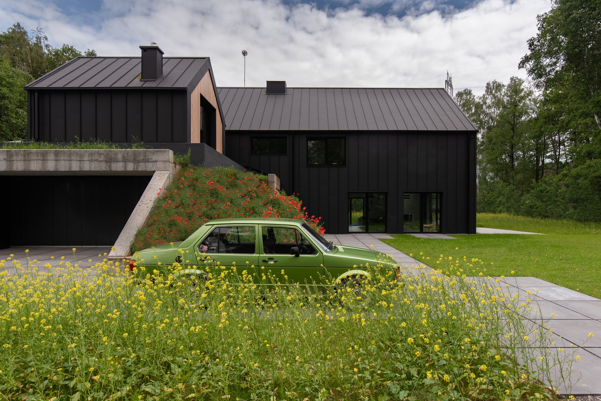 Volkswagen Golf parked beside modern house set into a landscaped hillside with wildflowers