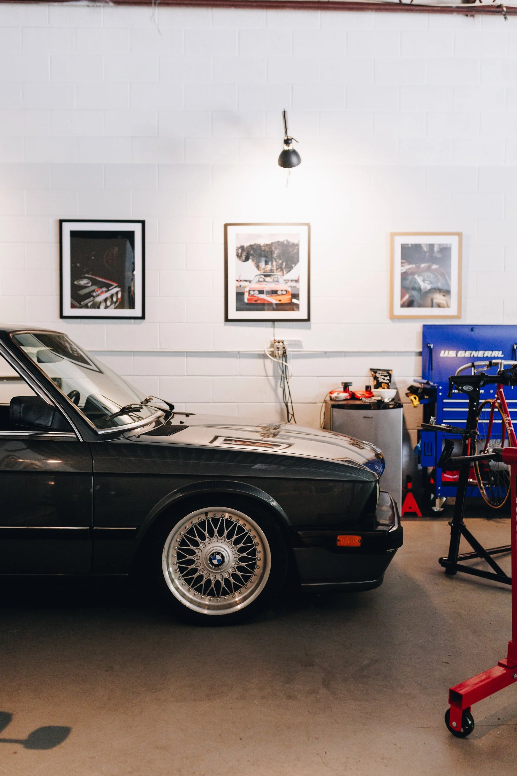 Classic BMW car in a garage with automotive equipment and framed pictures on the wall.