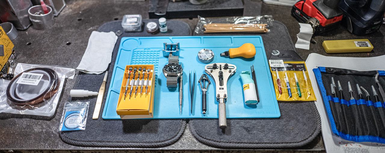 Workbench with tools, Seiko watch, and a blue mat on a cluttered surface